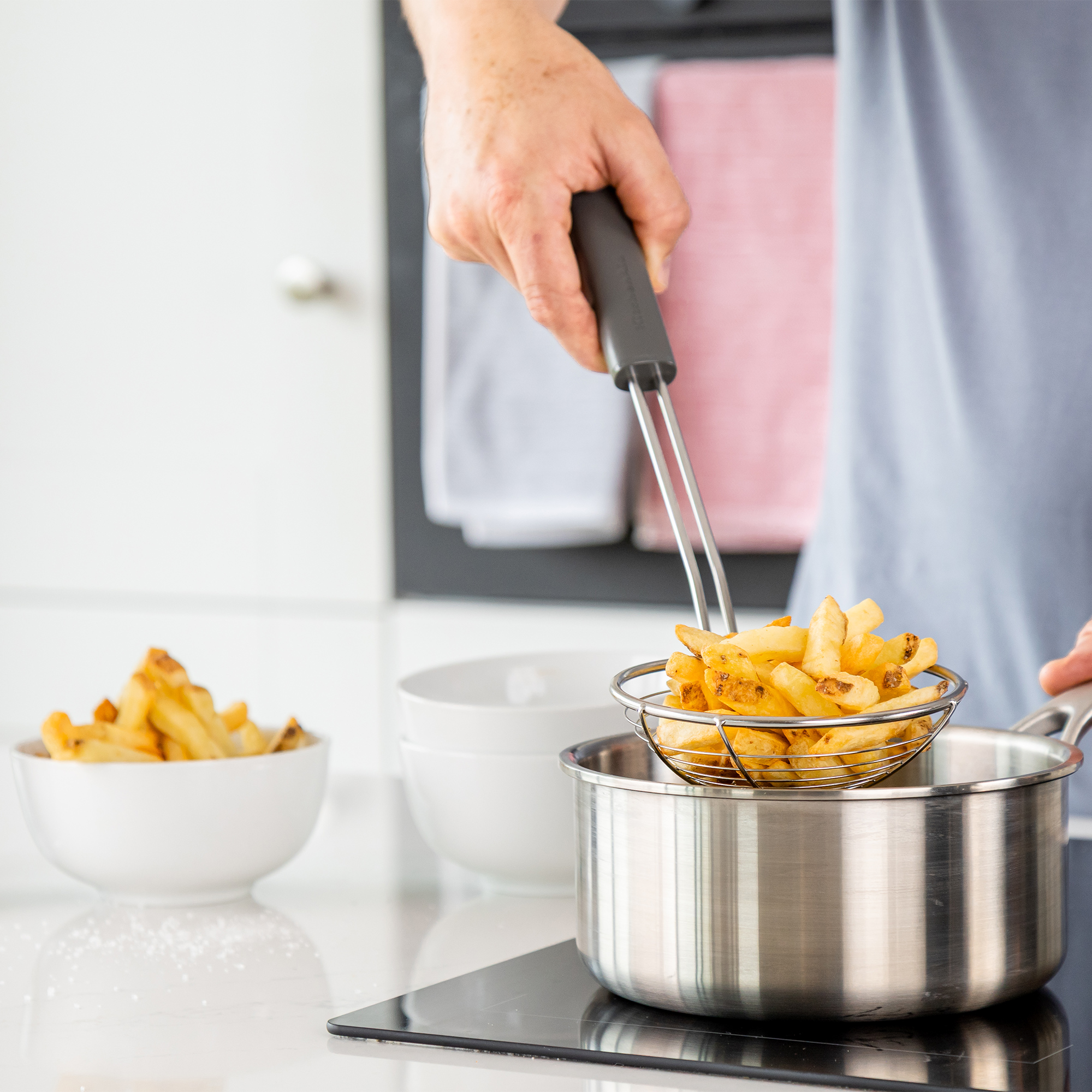 Ein Sieb mit goldbraunen Pommes wird aus einem Topf gehoben.