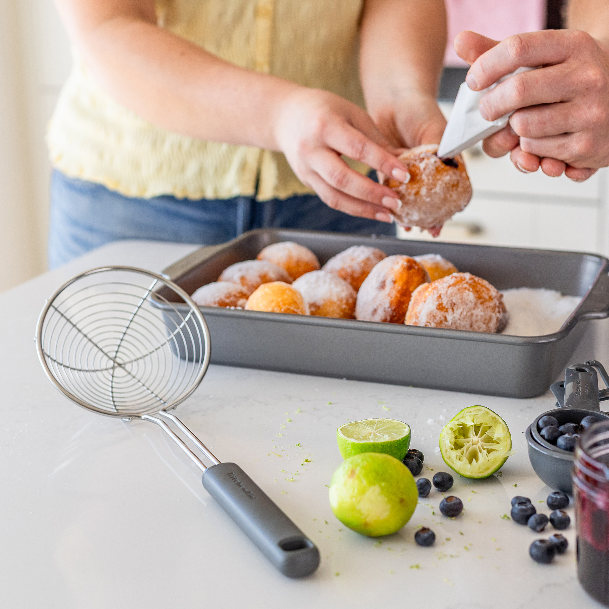 Zwei Personen verzieren frisch frittierte, in Zucker gewälzte Teigbällchen mit Füllung.
