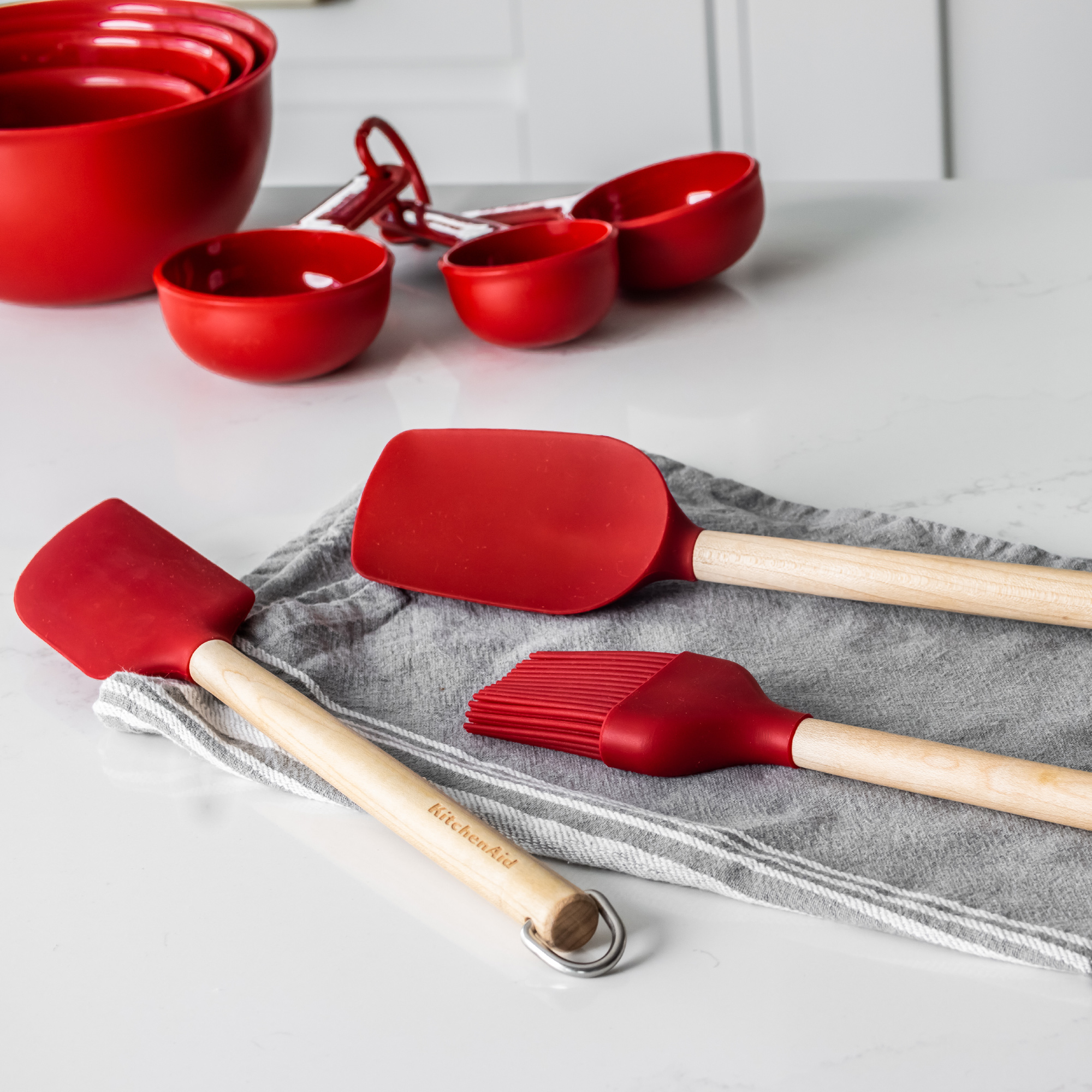 Rote Silikon-Küchenutensilien mit Holzgriffen auf grauem Streifentuch.
