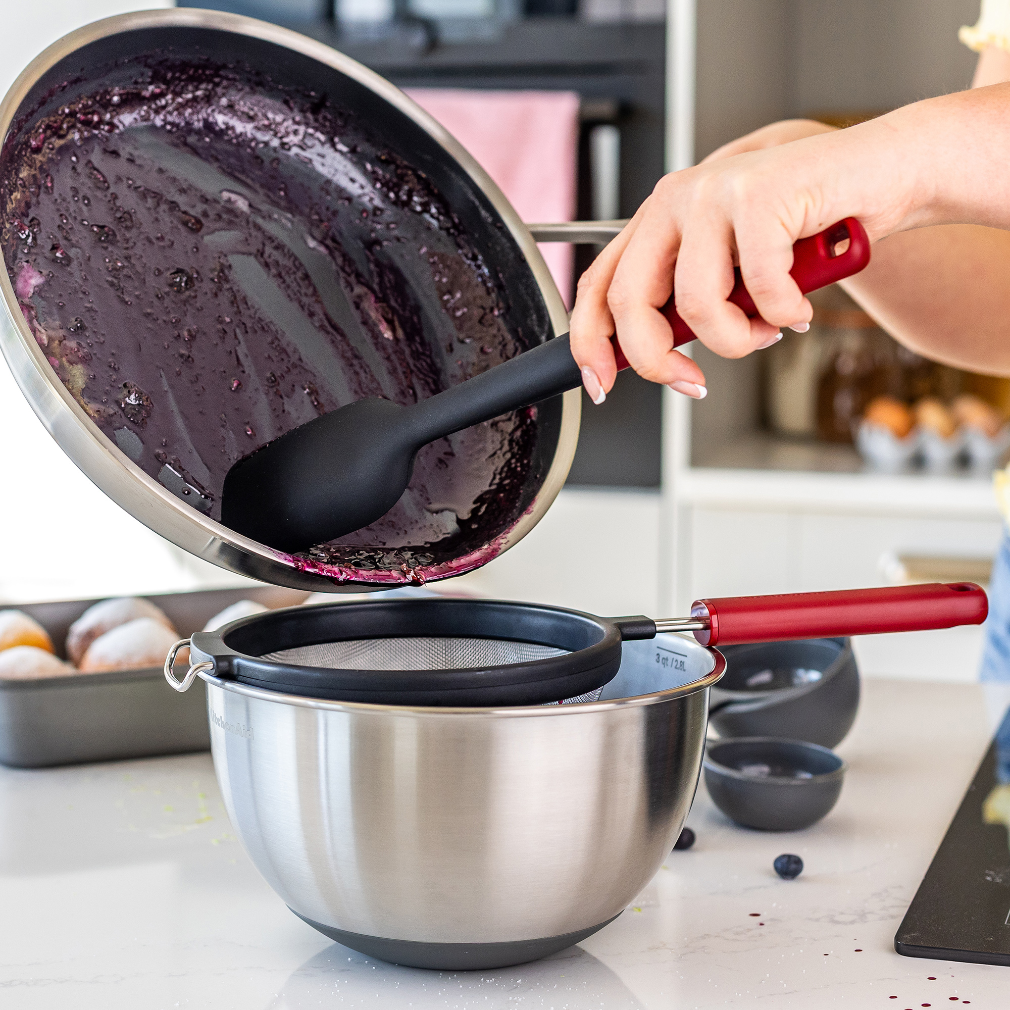Blaubeersauce wird aus einer Pfanne in ein Sieb über einer Schüssel gegossen.