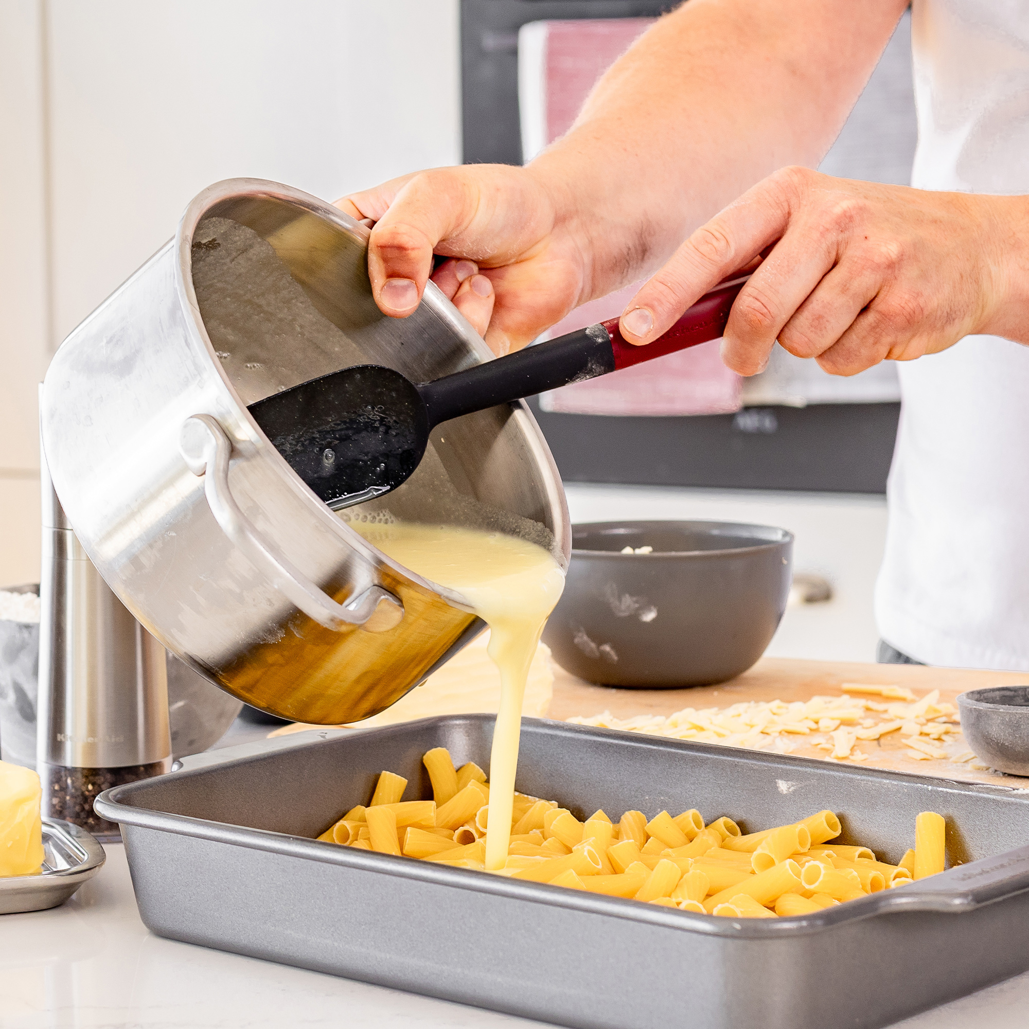 Flüssigkeit wird aus einem Topf über Rigatoni in eine Auflaufform gegossen.