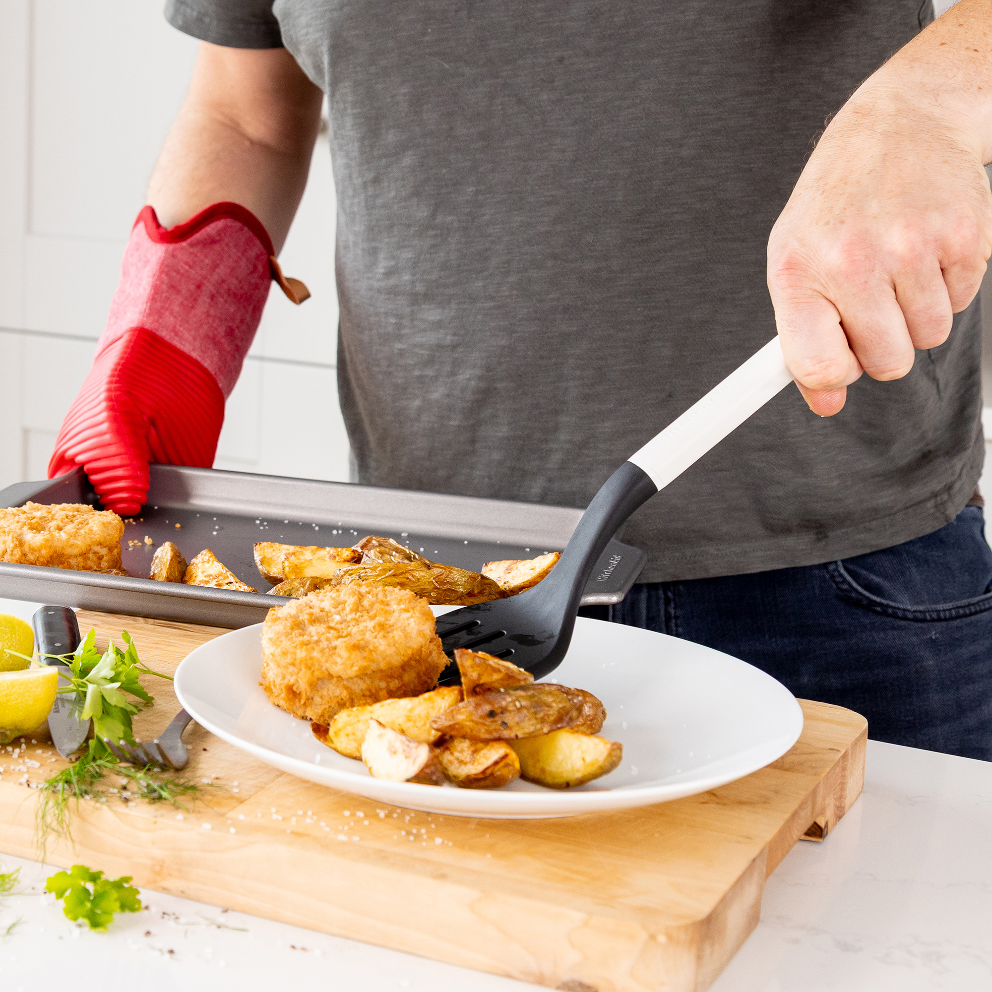 Person richt gebratenes Essen und Kartoffeln vom Backblech auf einen weißen Teller.