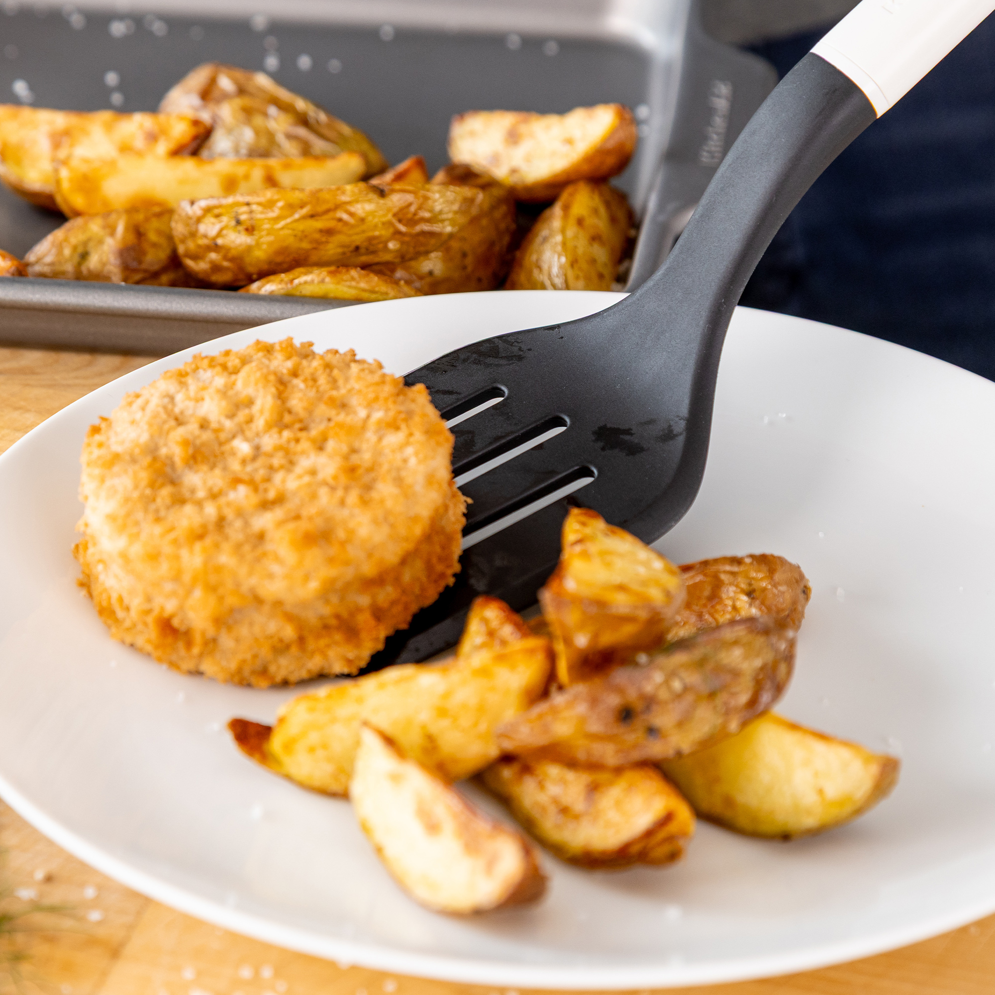 Ein paniertes Bratling und Kartoffelspalten werden auf einen Teller gelegt.
