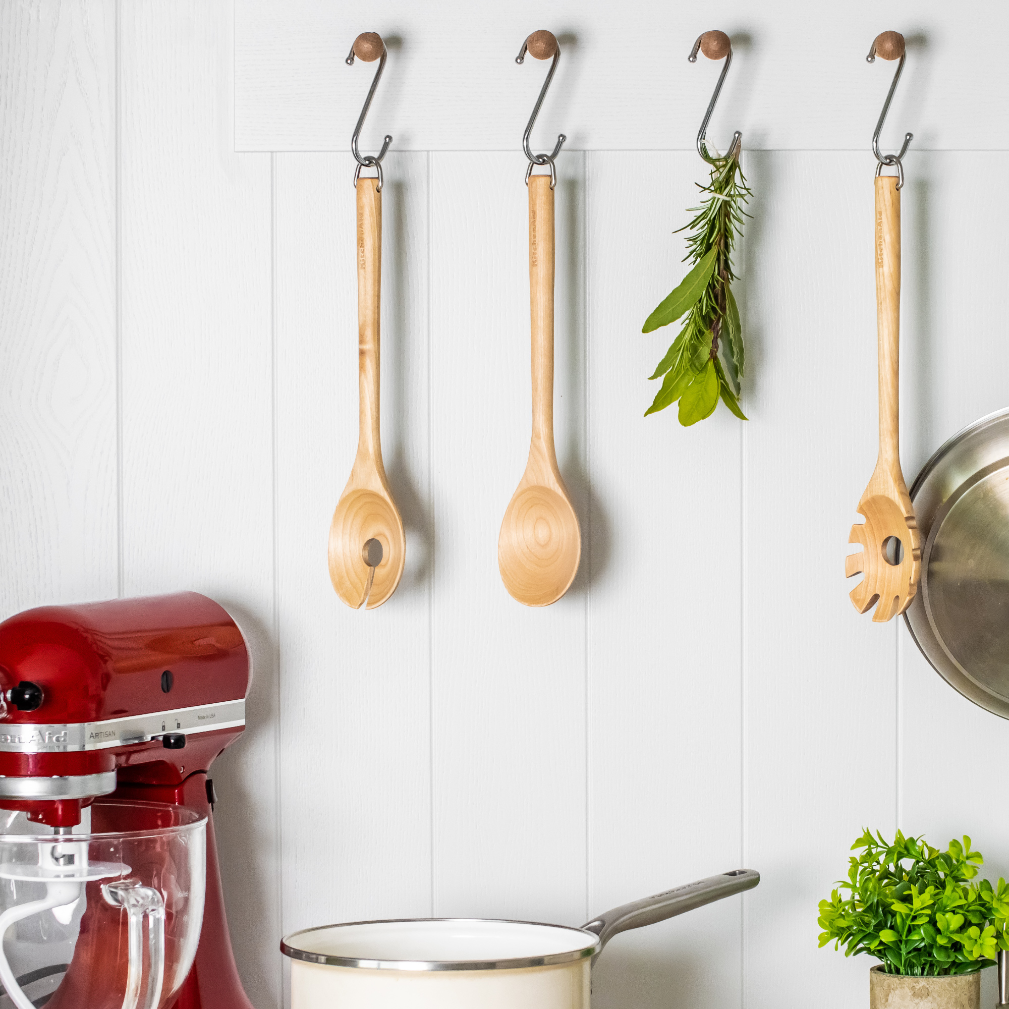 Küchenutensilien hängen an Haken: Rote Küchenmaschine, Holzlöffel, Kräuter.