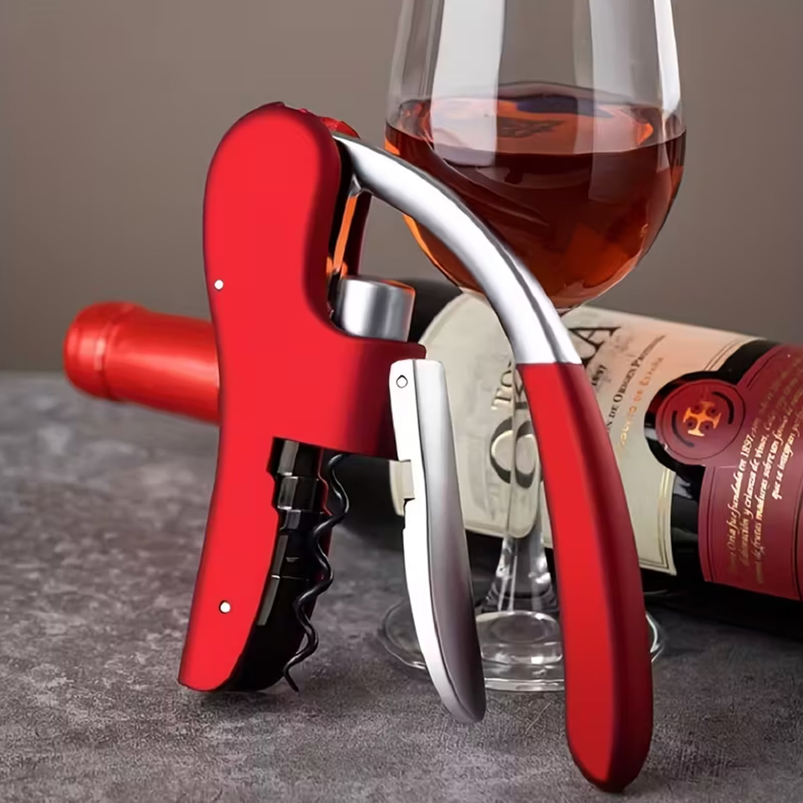 Ein roter Korkenzieher neben einer Weinflasche und einem Weinglas mit Rotwein.