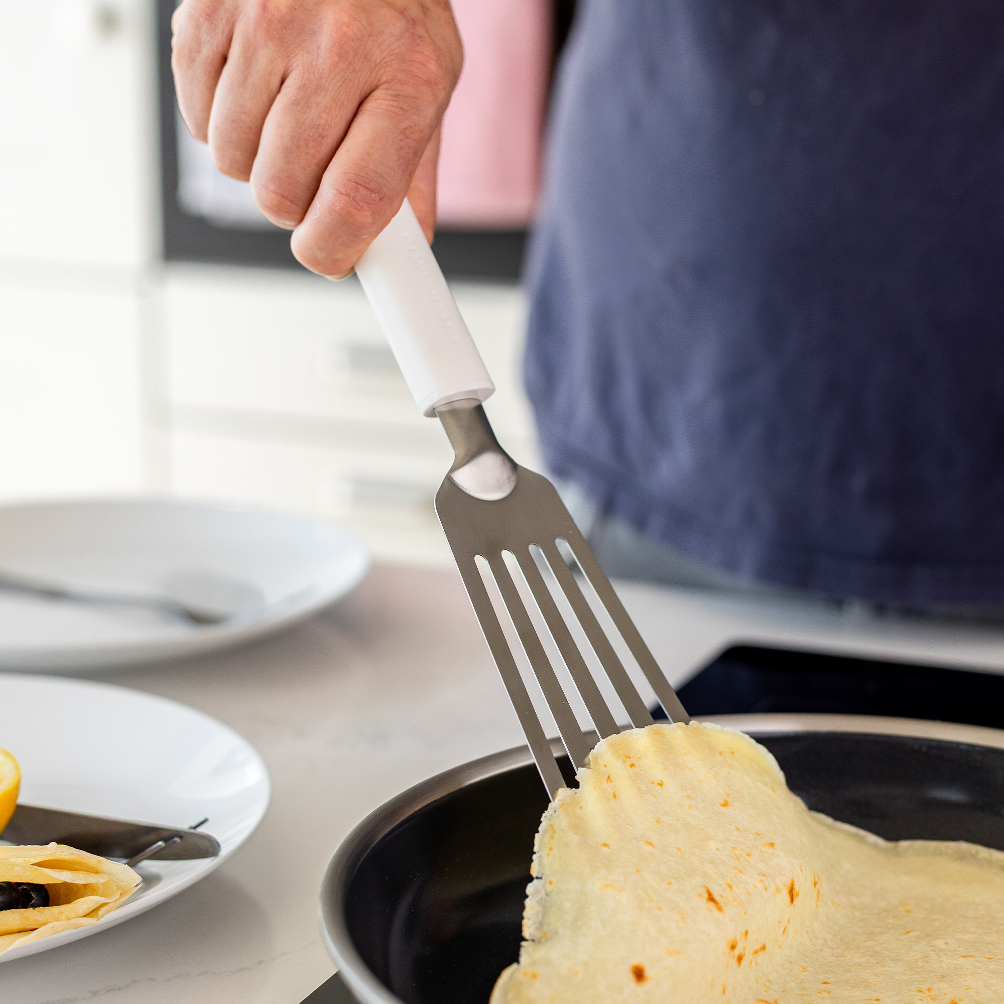 Eine Hand benutzt einen Spatel, um einen Pfannkuchen in einer Pfanne zu wenden.