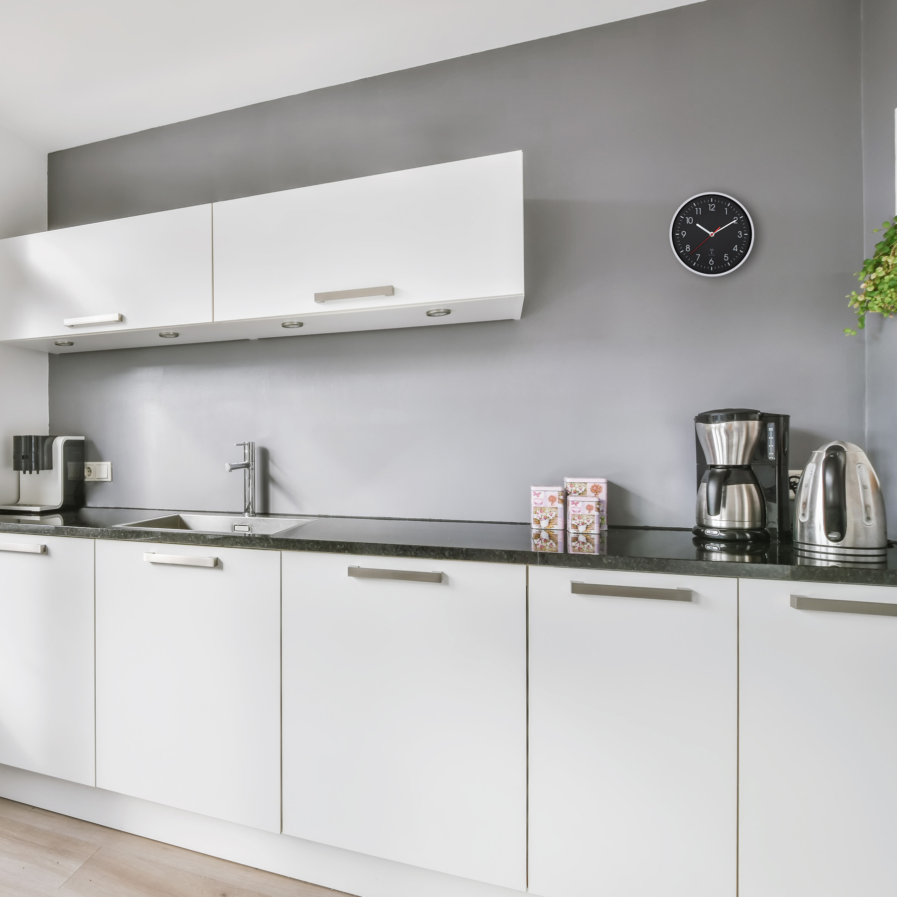 Moderne Küche mit weißen Schränken, schwarzer Arbeitsplatte, Kaffeemaschine und Wasserkocher.