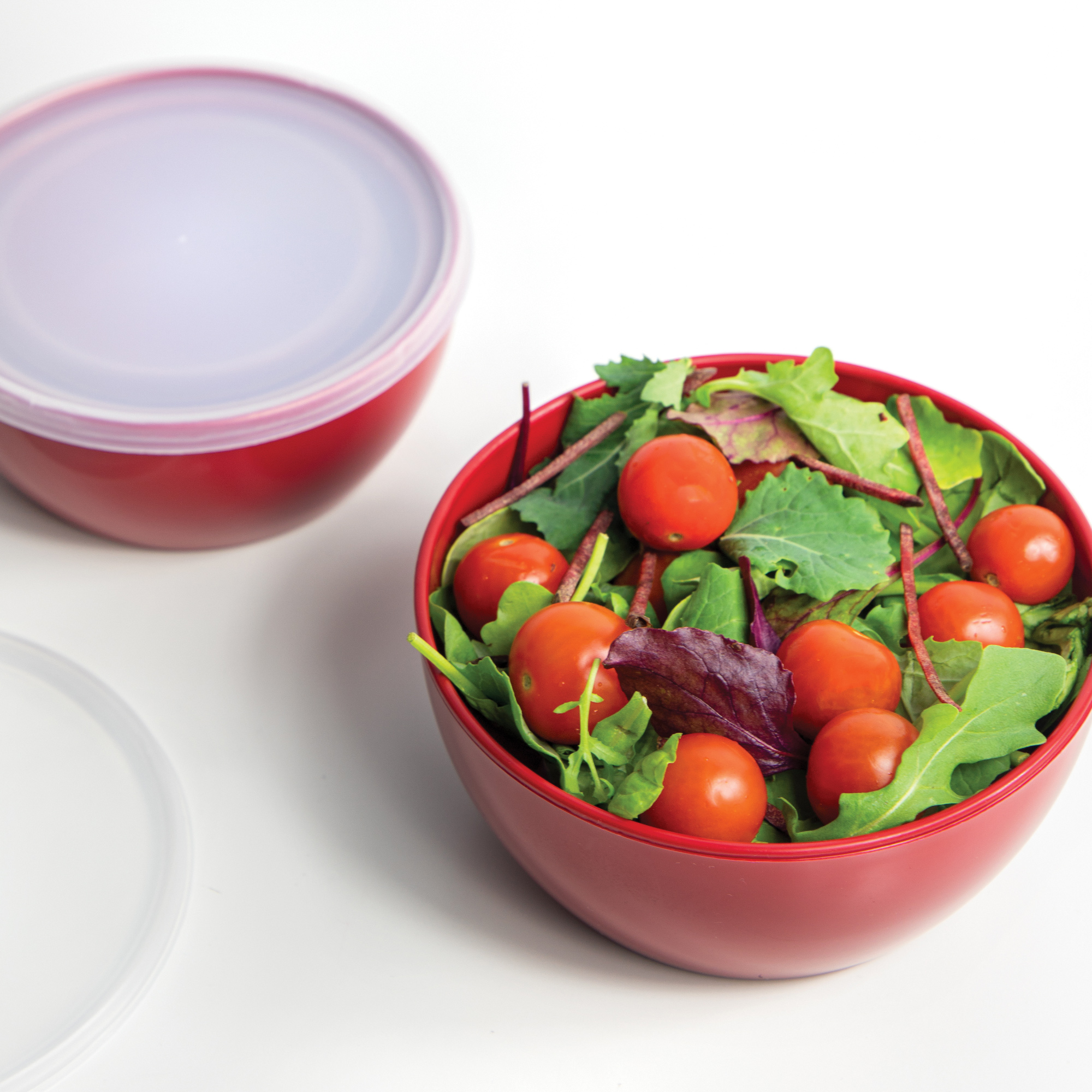 Roter Salatbehälter mit Deckel und frischem Salat mit Tomaten.