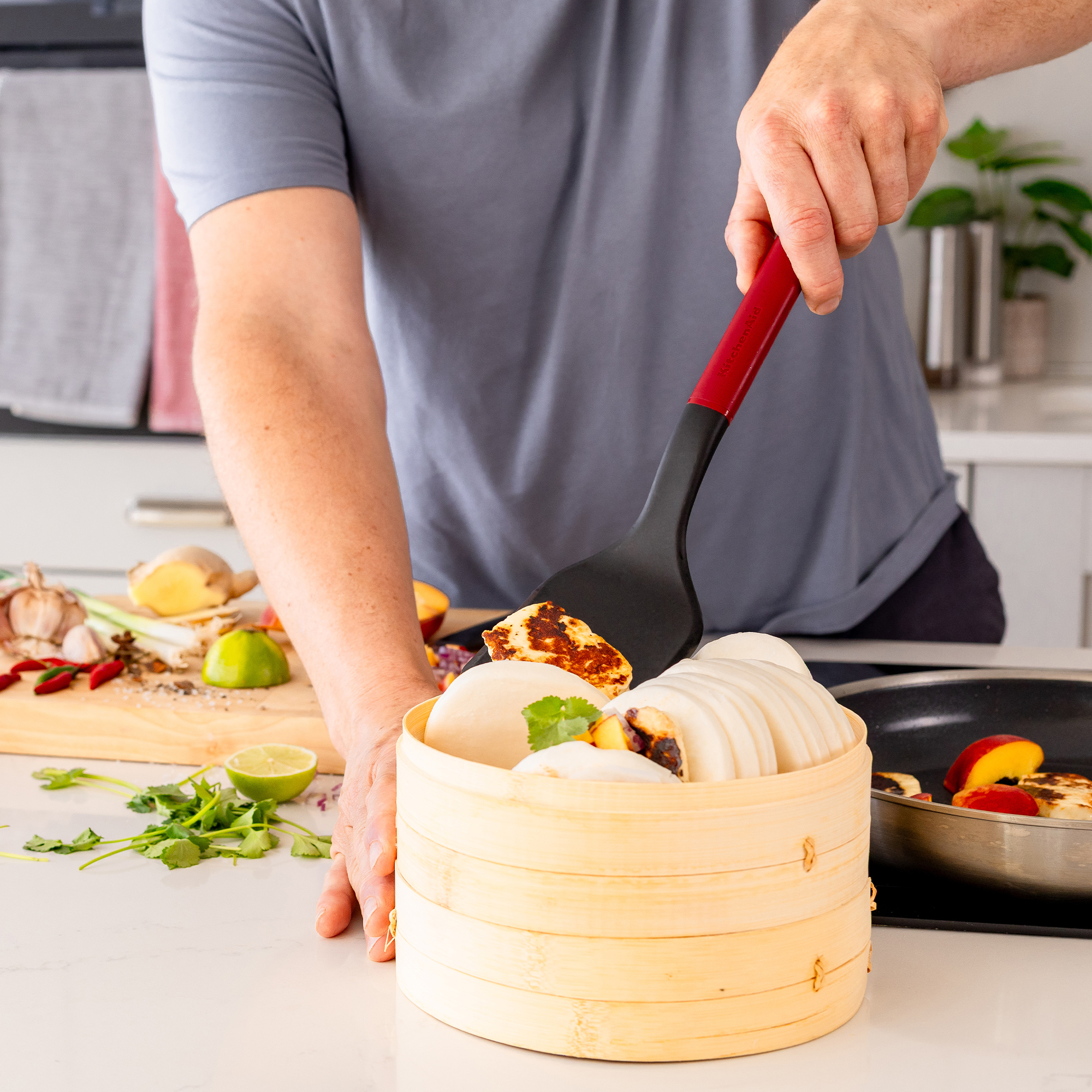 Ein Koch hebt mit einem Spatel gebratenen Halloumi aus einem Bambusdämpfer.