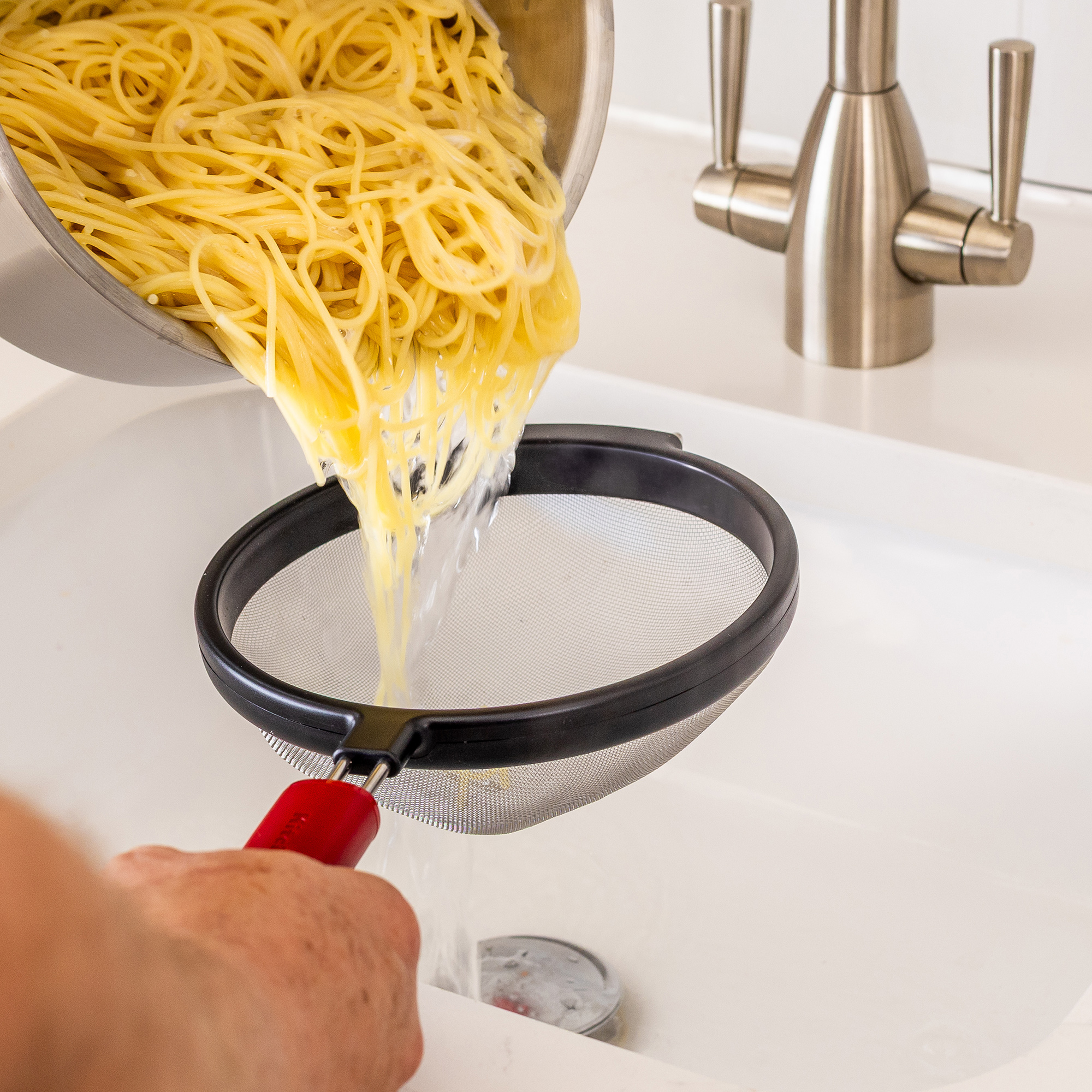 Spaghetti werden aus einem Topf in ein Sieb über einem Spülbecken abgetropft.