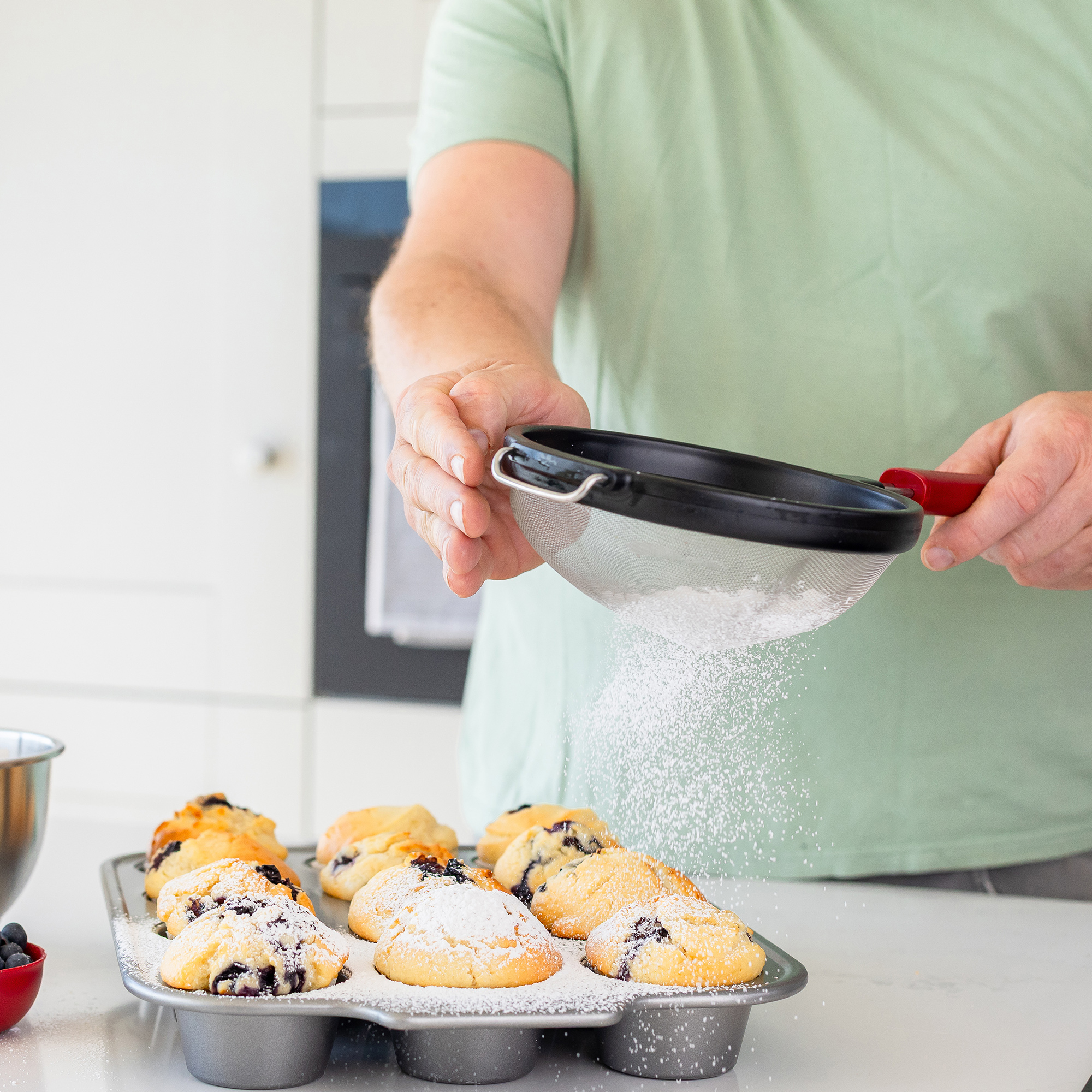 Puderzucker wird über Blaubeermuffins in einer Backform gesiebt.