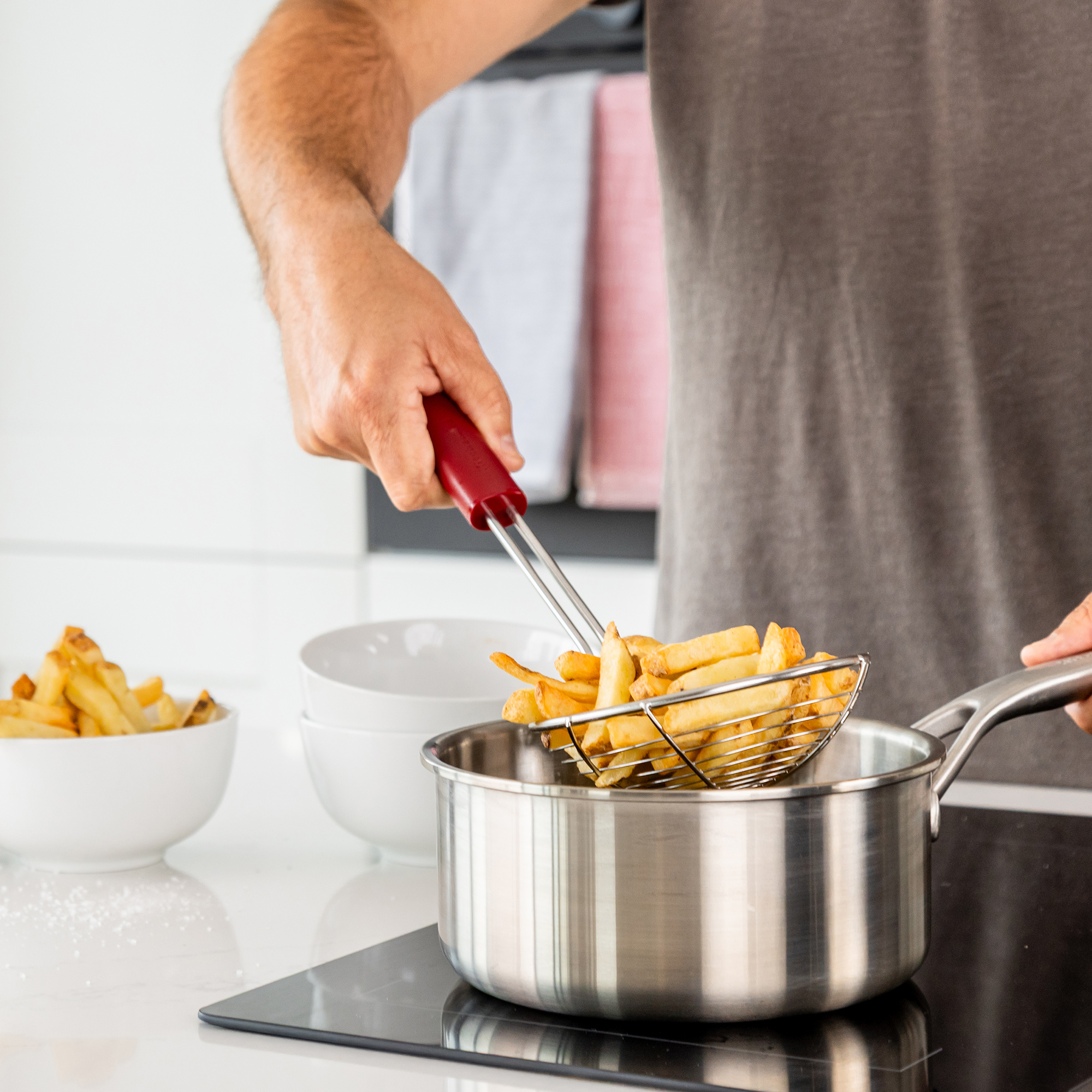 Ein Mann hebt einen Siebkorb mit Pommes Frites aus einem Topf.