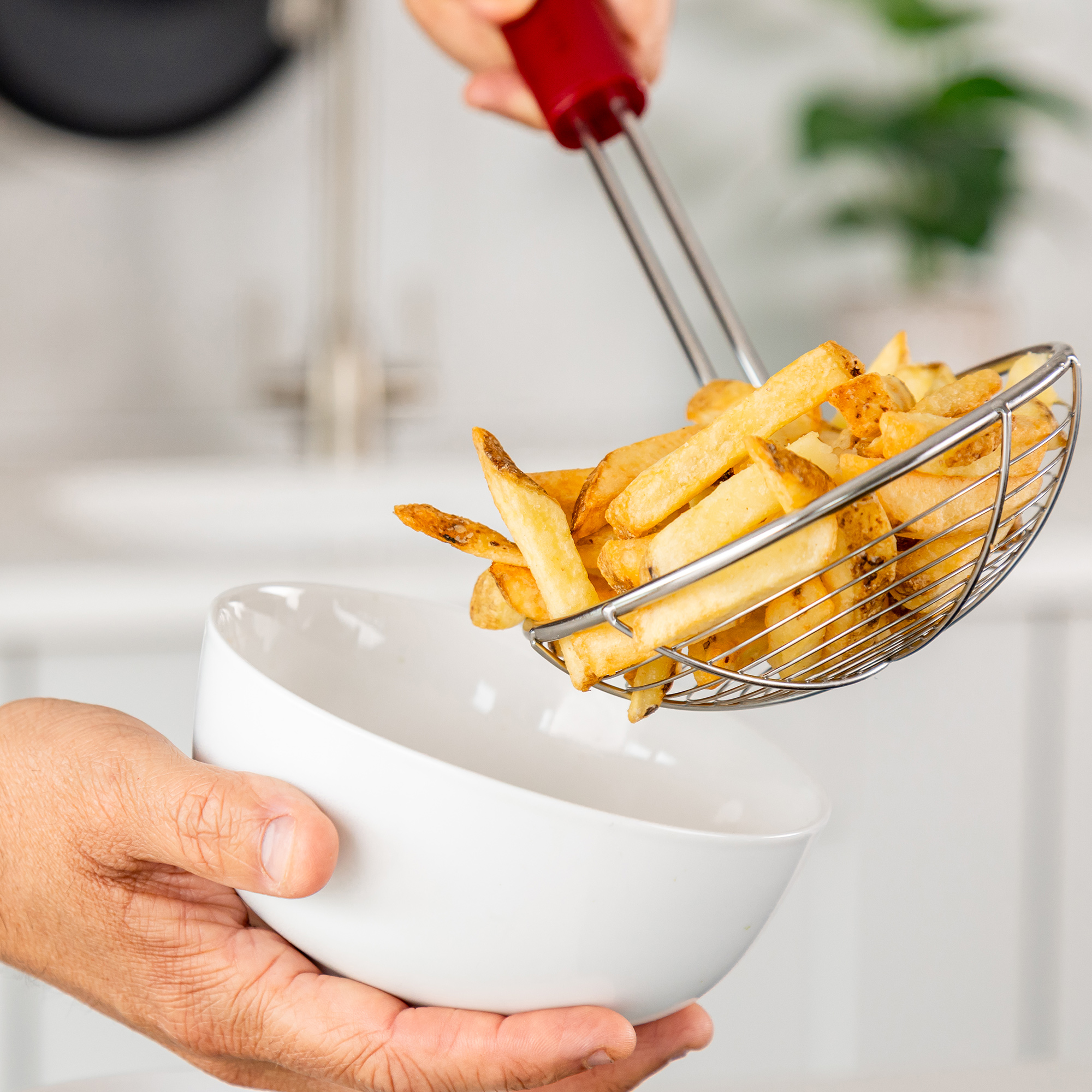 Pommes Frites werden mit einem Sieb in eine weiße Schüssel gegeben.