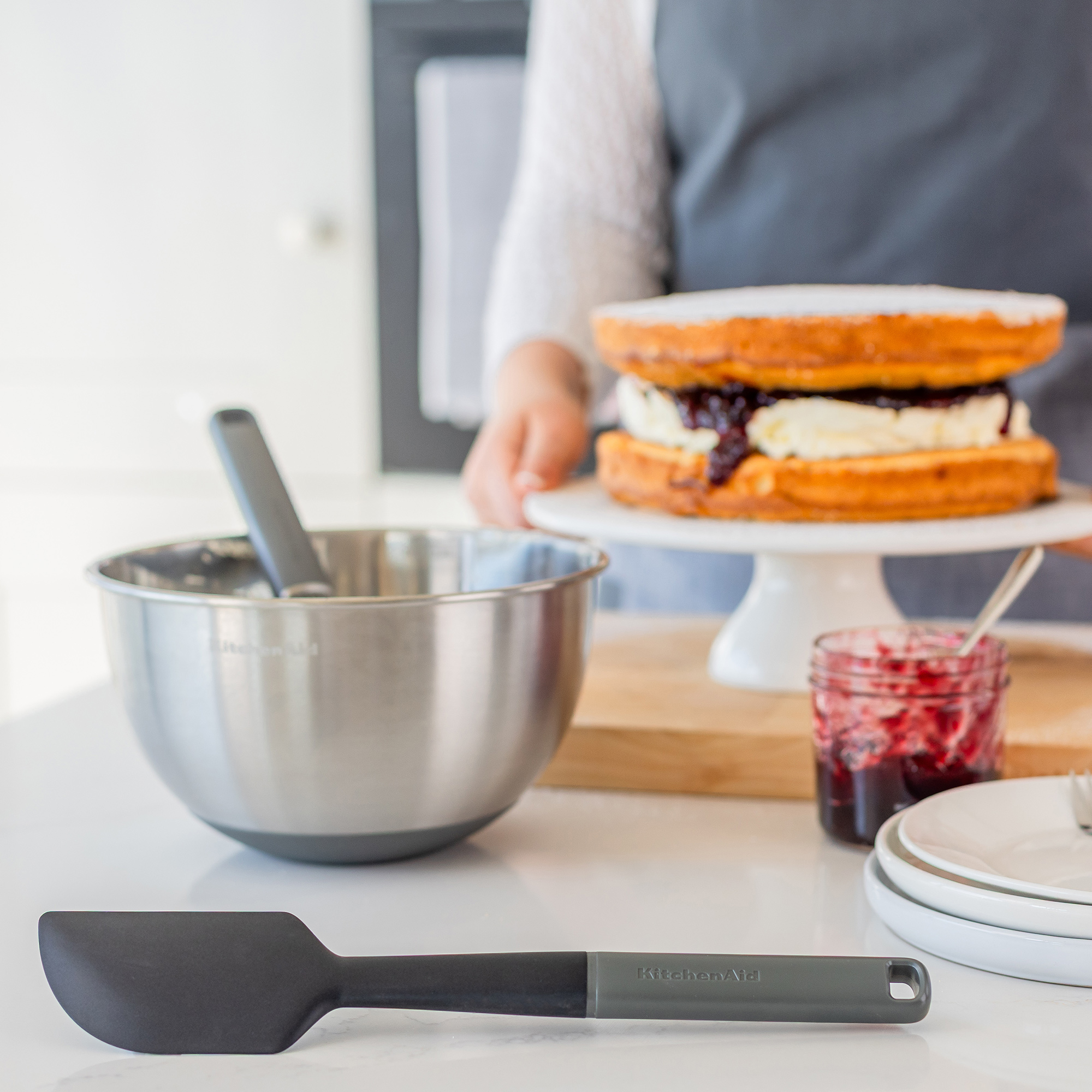 Eine Person schichtet einen Kuchen mit Marmelade und Sahne auf einem Kuchenteller.