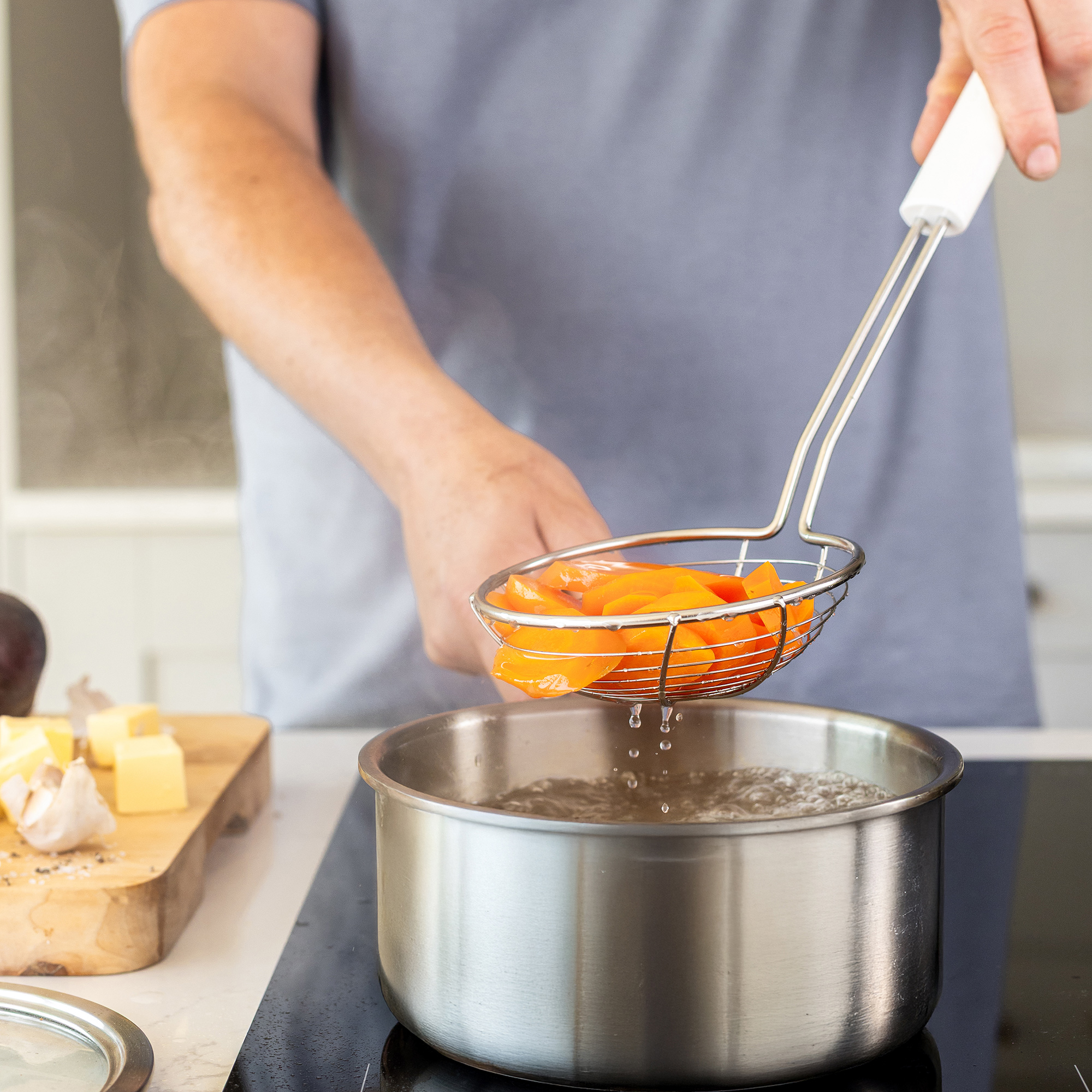 Orangefarbene Karottenstücke werden mit einem Sieblöffel aus kochendem Wasser gehoben.