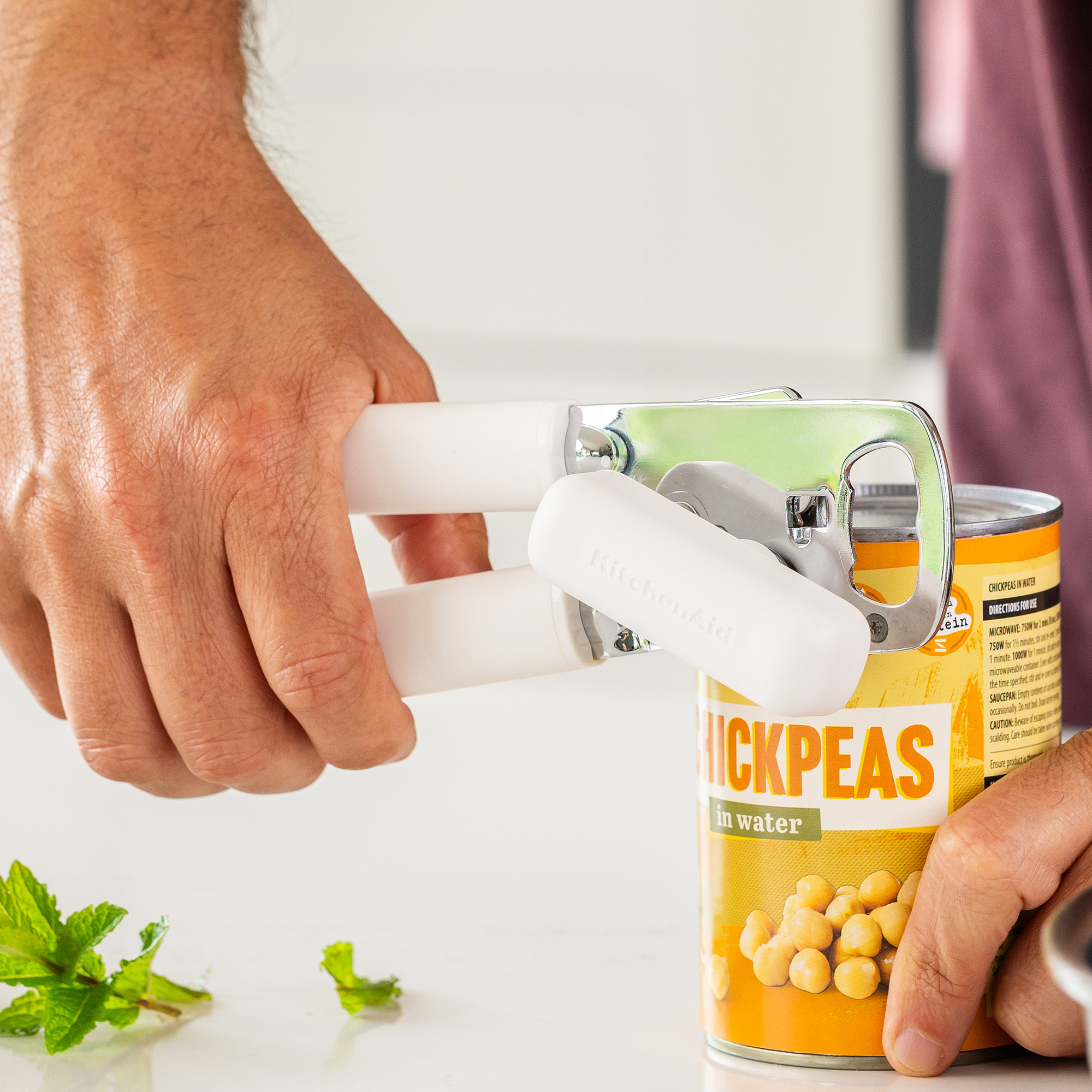 Eine Hand benutzt einen weißen Dosenöffner, um eine Dosen-Kichererbsen zu öffnen.
