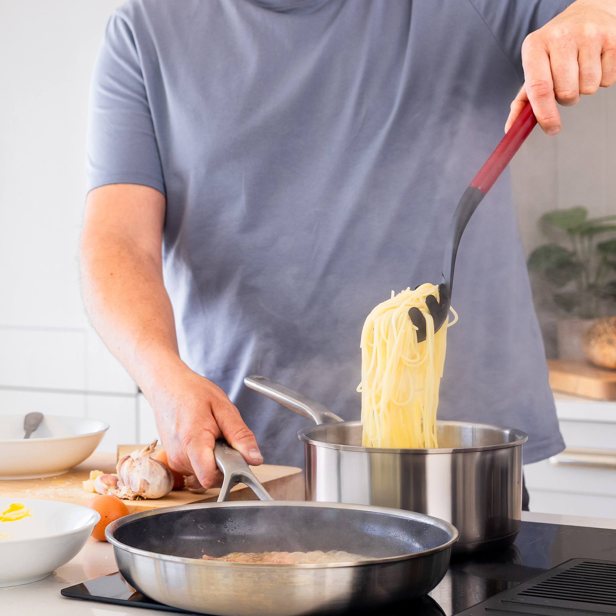Ein Mann kocht Spaghetti in einem Topf und brät etwas in einer Pfanne an.