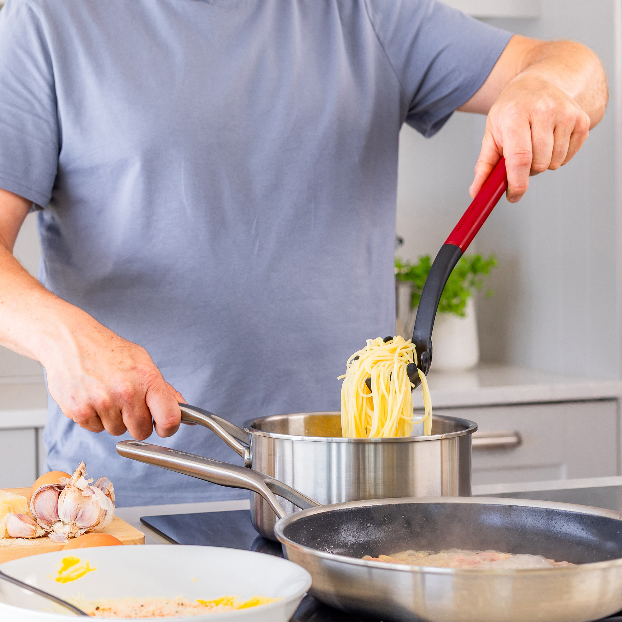 Eine Person kocht Spaghetti in einem Topf und legt sie in eine Pfanne.