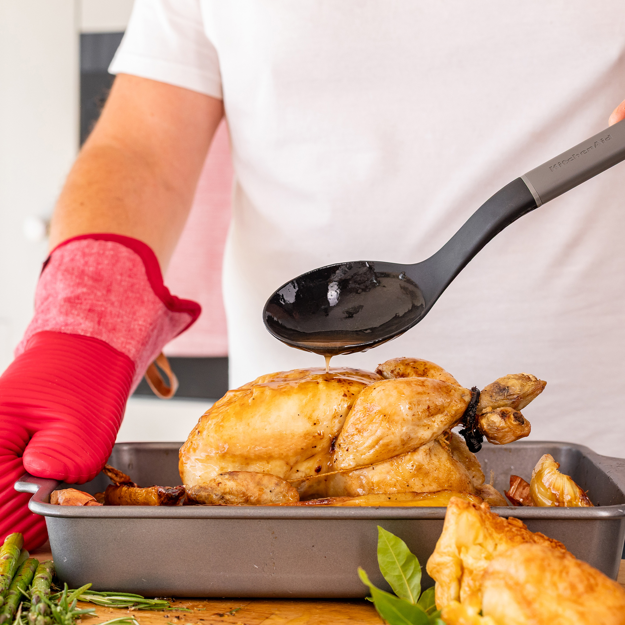 Eine Person übergießt ein Brathähnchen mit Sauce aus einem Löffel.