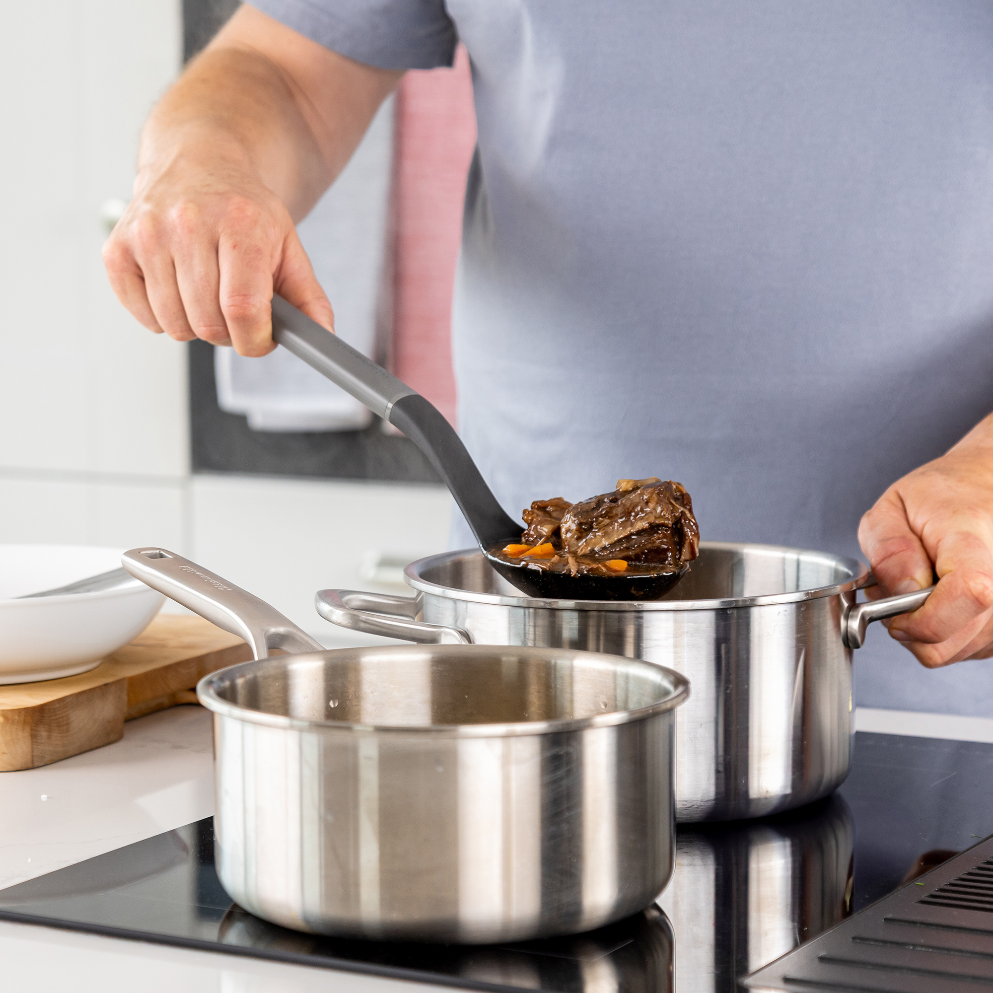 Eine Person hebt mit einem Löffel ein Stück Fleisch und Karotten aus einem Topf.