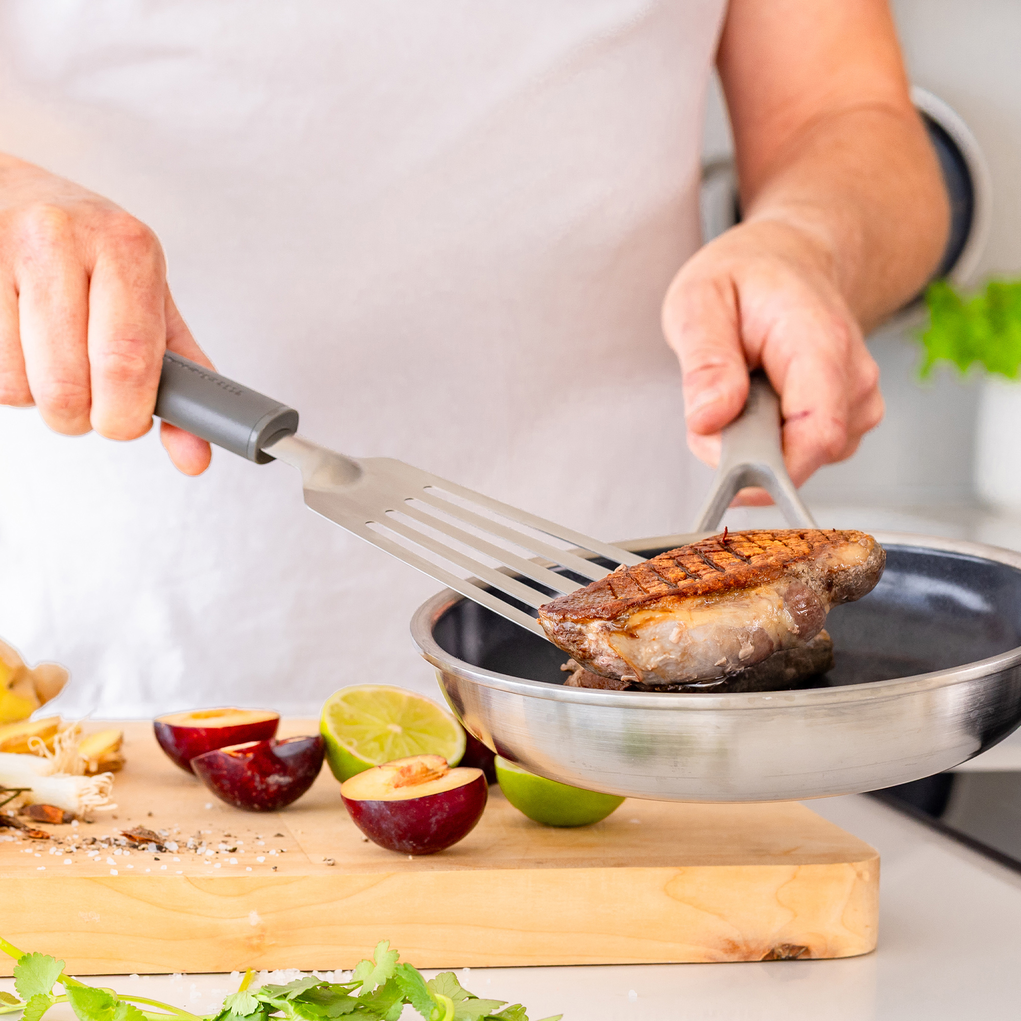 Gebratene Entenbrust wird mit einem Spatel aus einer Pfanne gehoben, daneben liegen Früchte.
