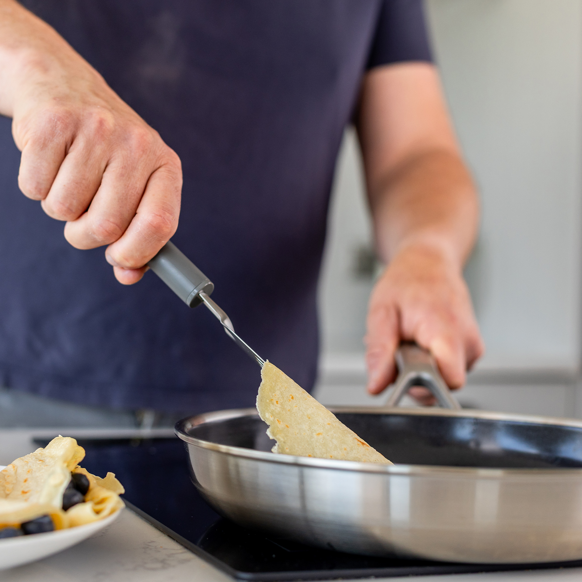Eine Person wendet einen Pfannkuchen in einer Pfanne mit einem Werkzeug.