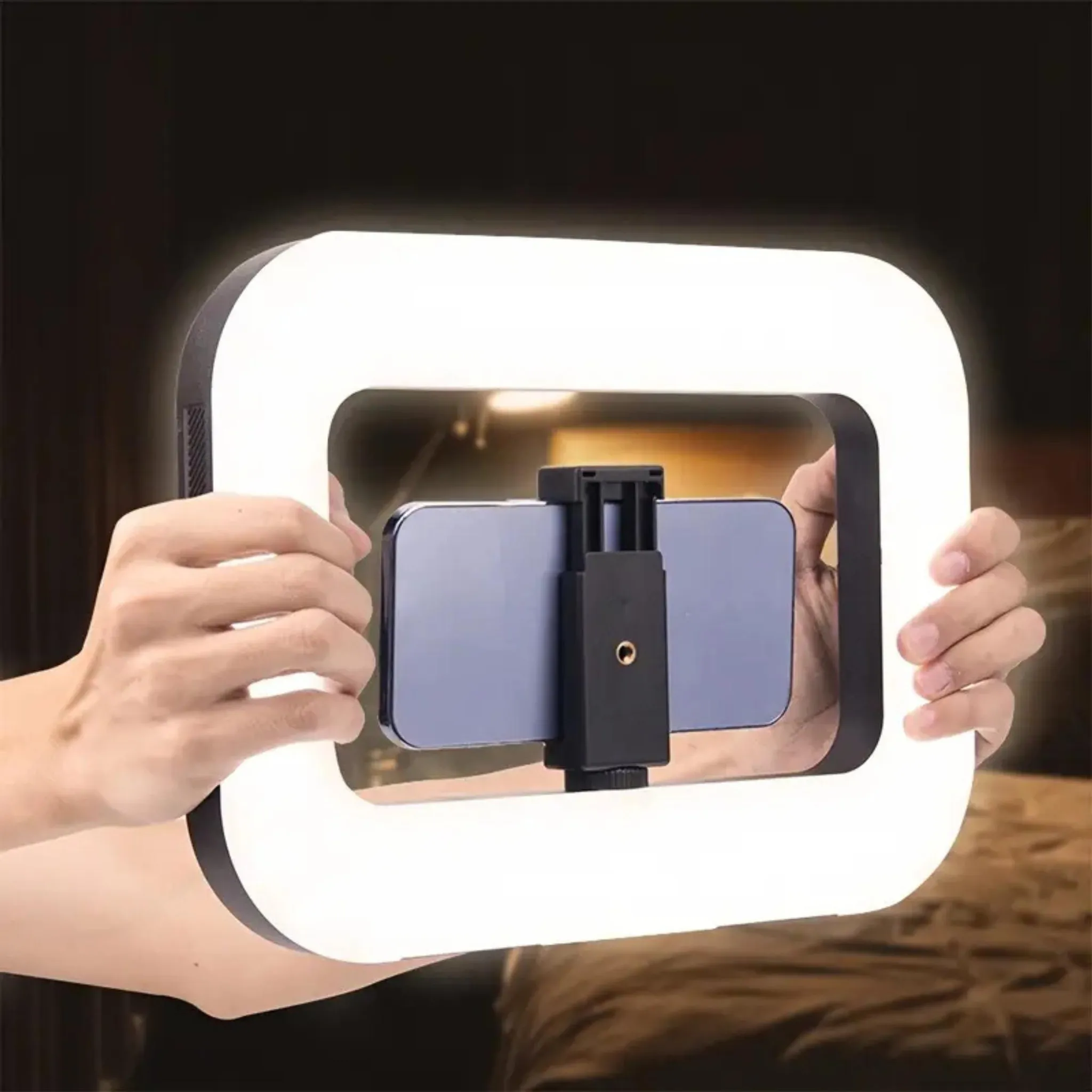 Eine rechteckige Ringlichtlampe mit einem Smartphone-Halter in der Mitte wird von Händen gehalten.