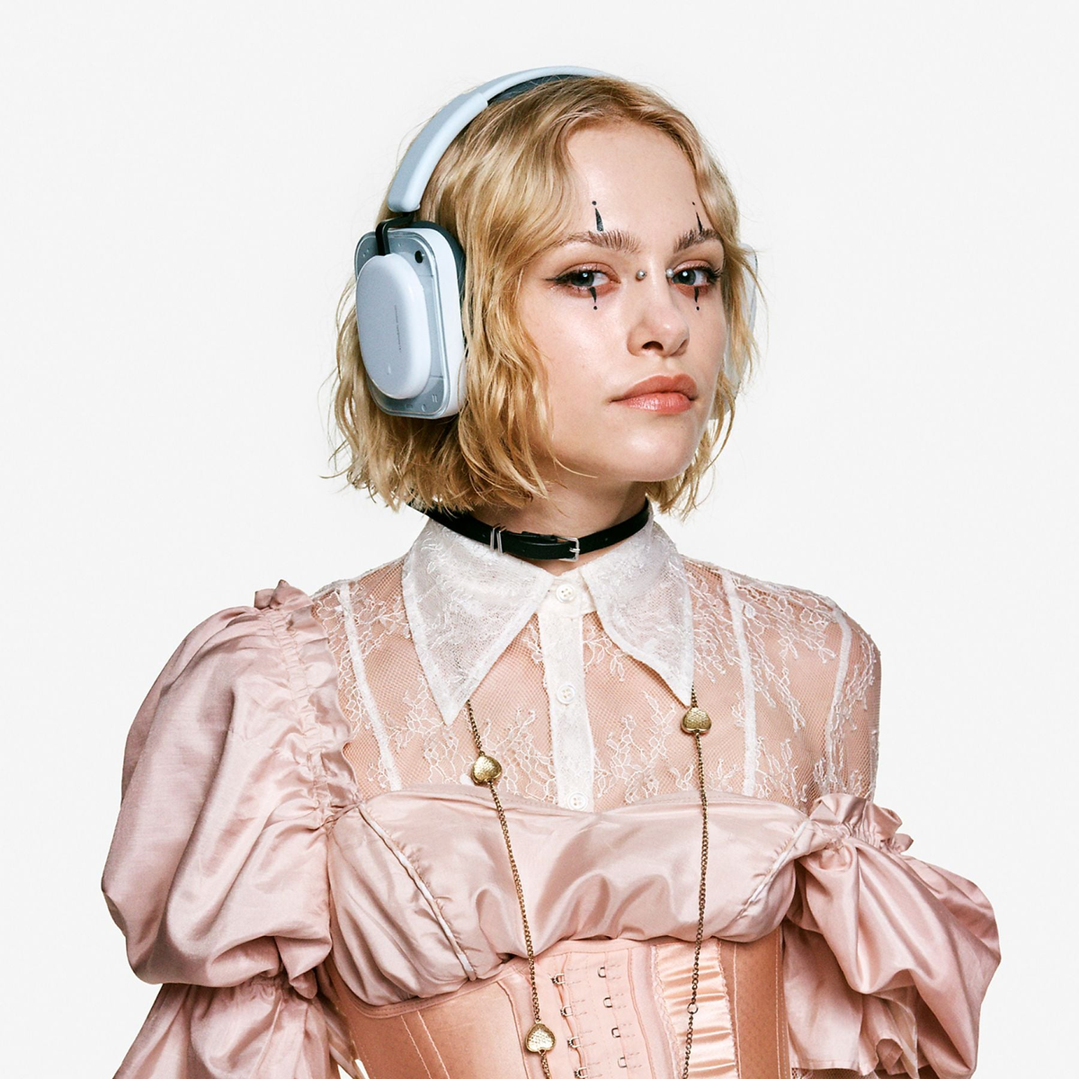 Una donna bionda indossa cuffie, un choker nero e un corsetto rosa.