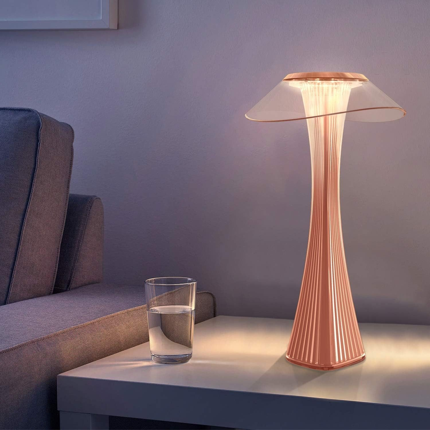 Una moderna lampada color rame con vetro e un bicchiere d'acqua su un tavolo.