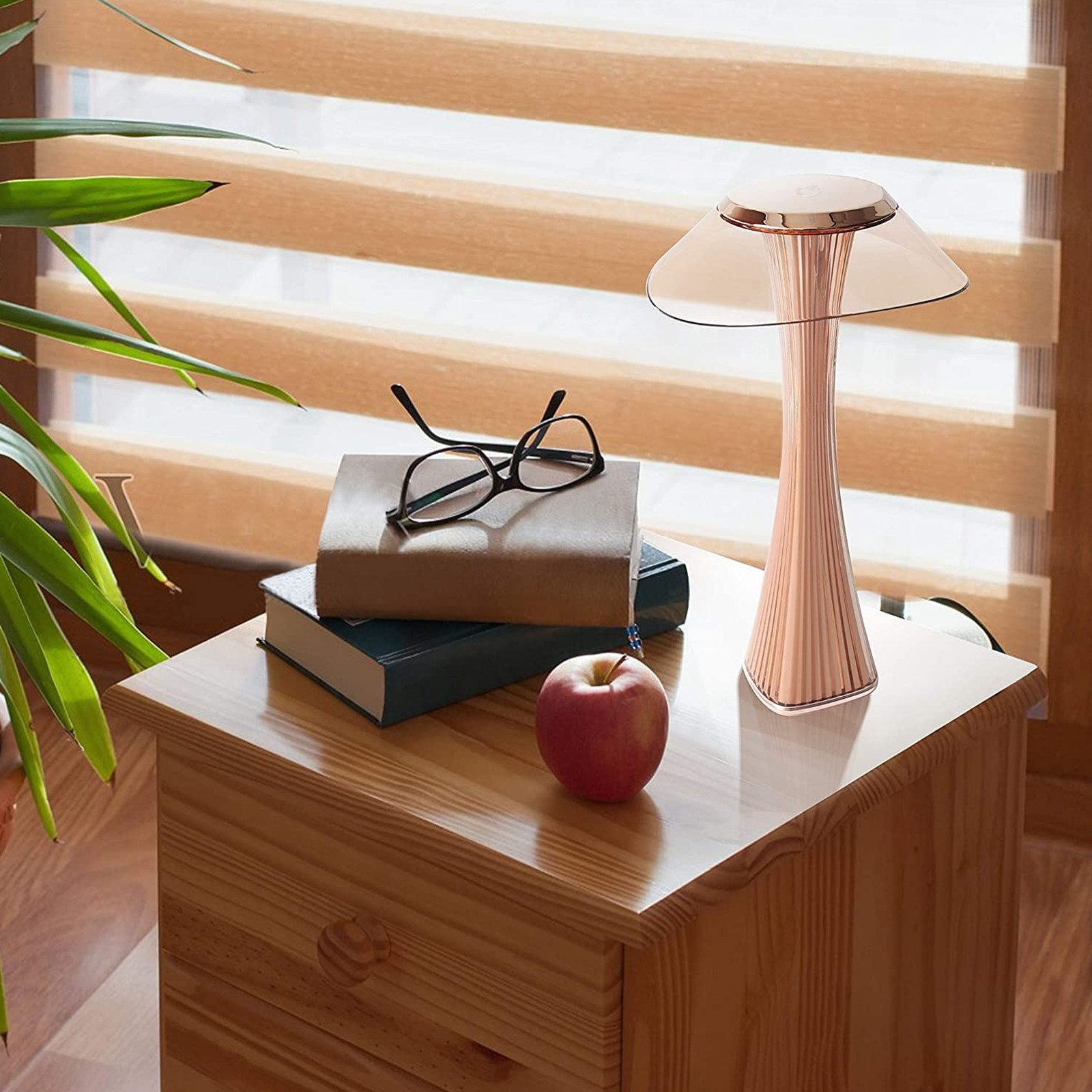 Un comodino con lampada, libri, occhiali e mela.