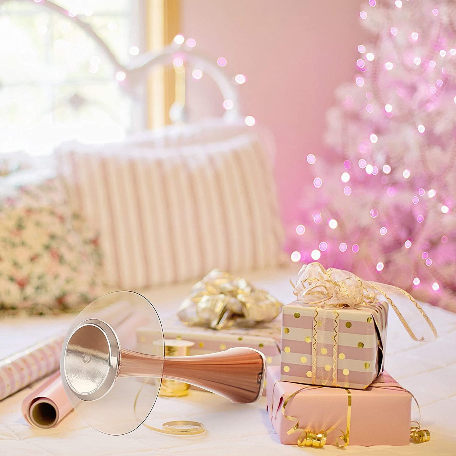 Regali con nastri rosa e oro, un albero di Natale con luci.
