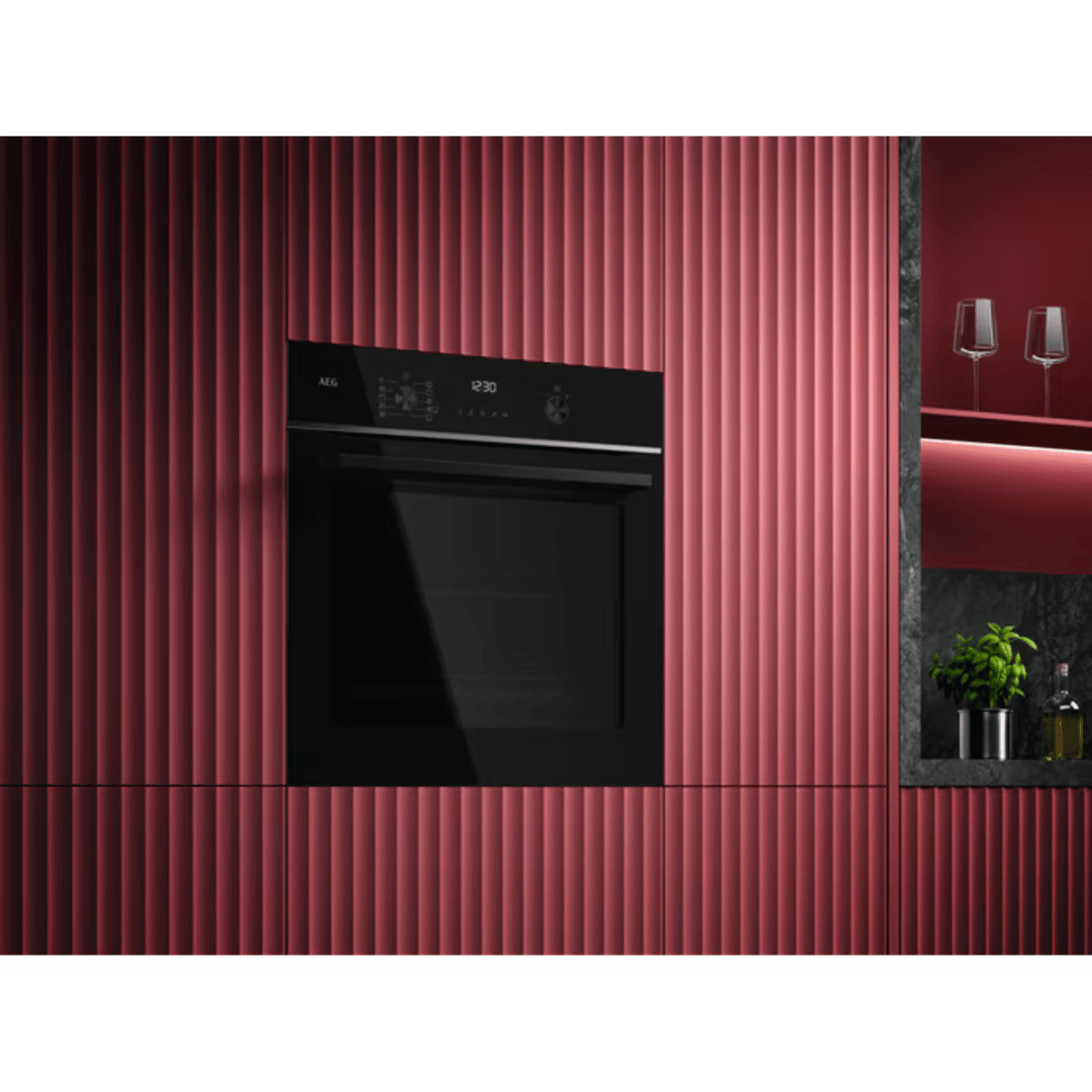 Czarny piekarnik jest osadzony w czerwonej, prążkowanej szafce. Dwa kieliszki do wina i roślina stoją na półce.