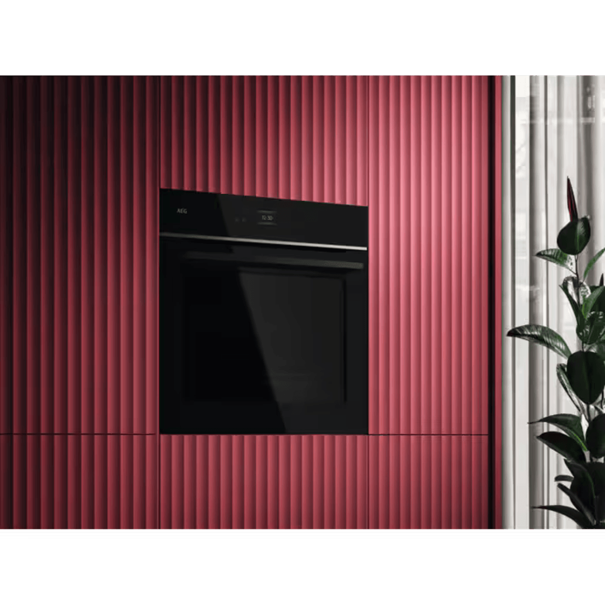 Piekarnik do zabudowy w czerwonej, żłobionej zabudowie kuchennej z rośliną obok.