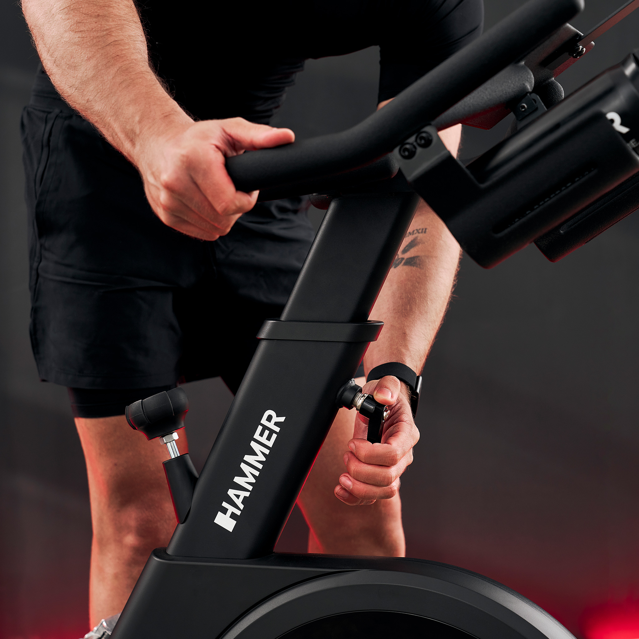 Mężczyzna reguluje opór czarnego roweru treningowego. Zbliżenie.