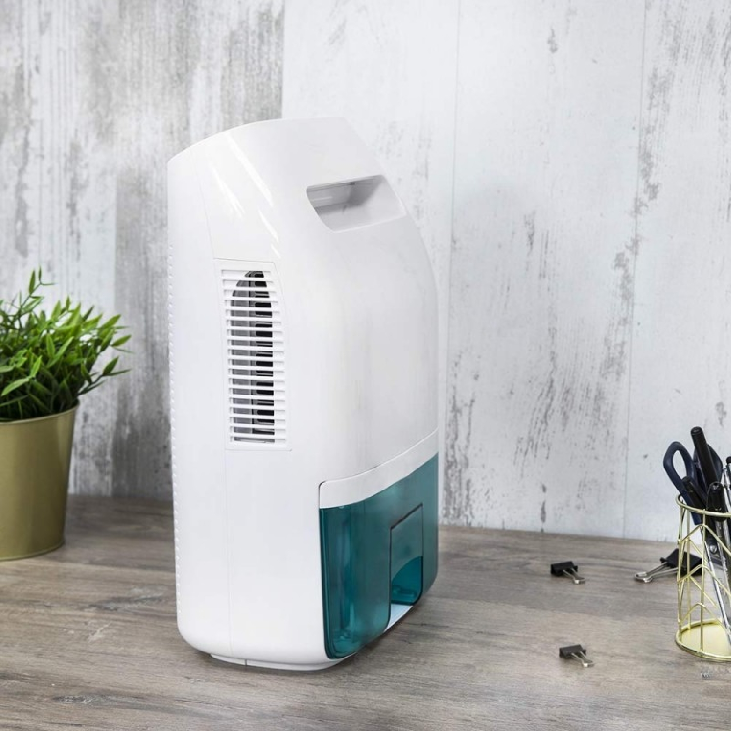 Biały osuszacz powietrza z niebieskim zbiornikiem stoi na drewnianym stole.