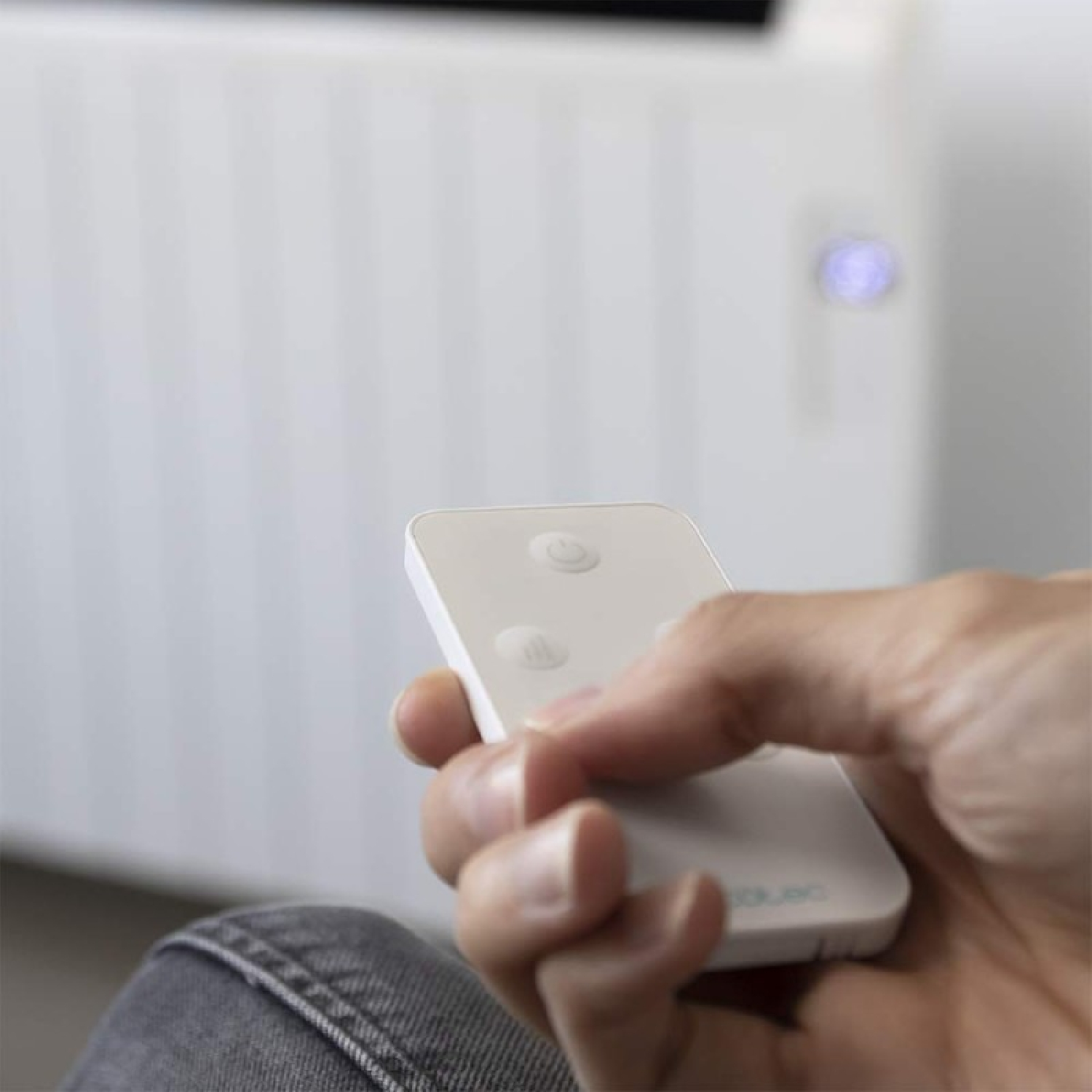 Dłoń trzymająca biały pilot, z białym grzejnikiem w tle.