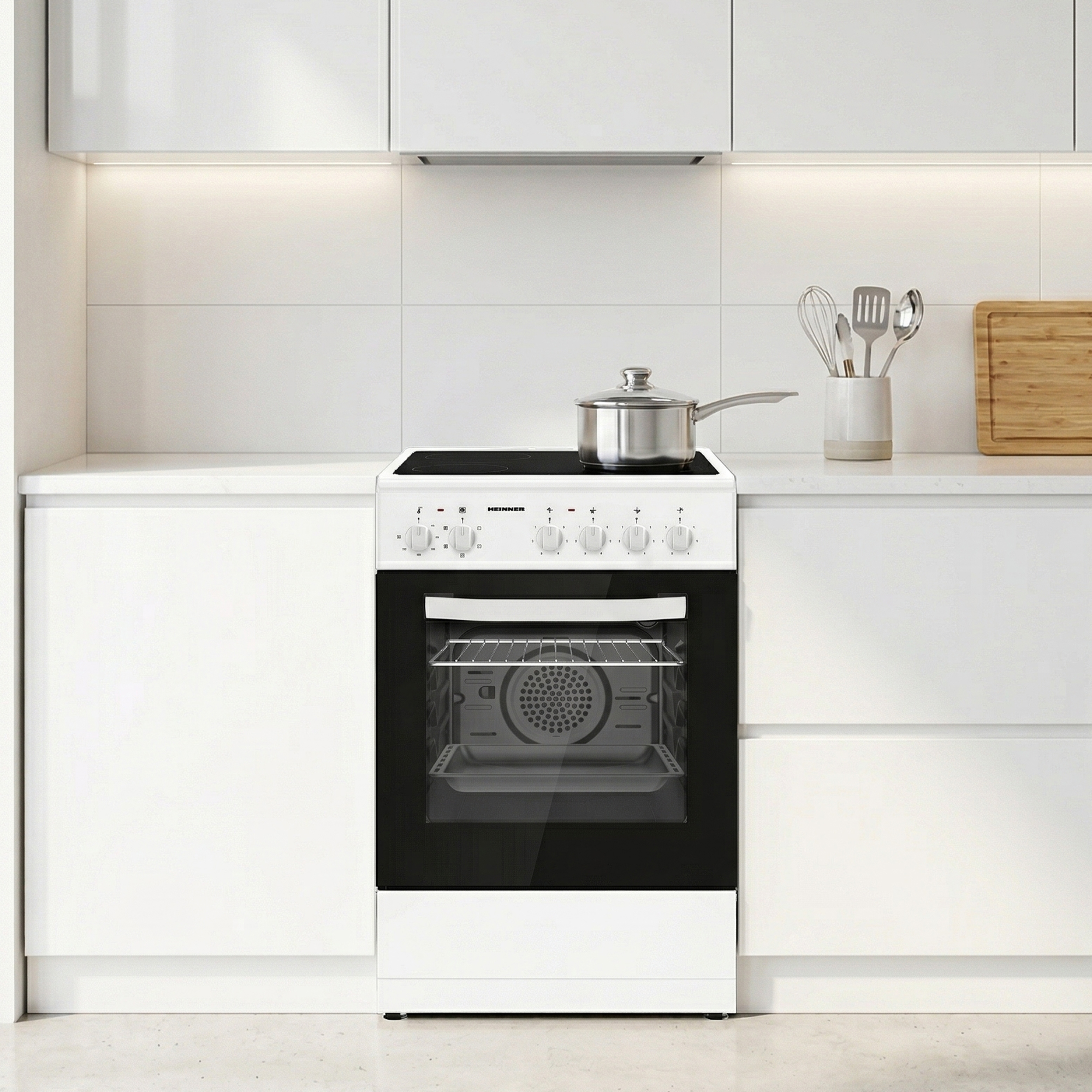 Een witte oven met een pan op de keramische kookplaat en keukengerei ernaast.