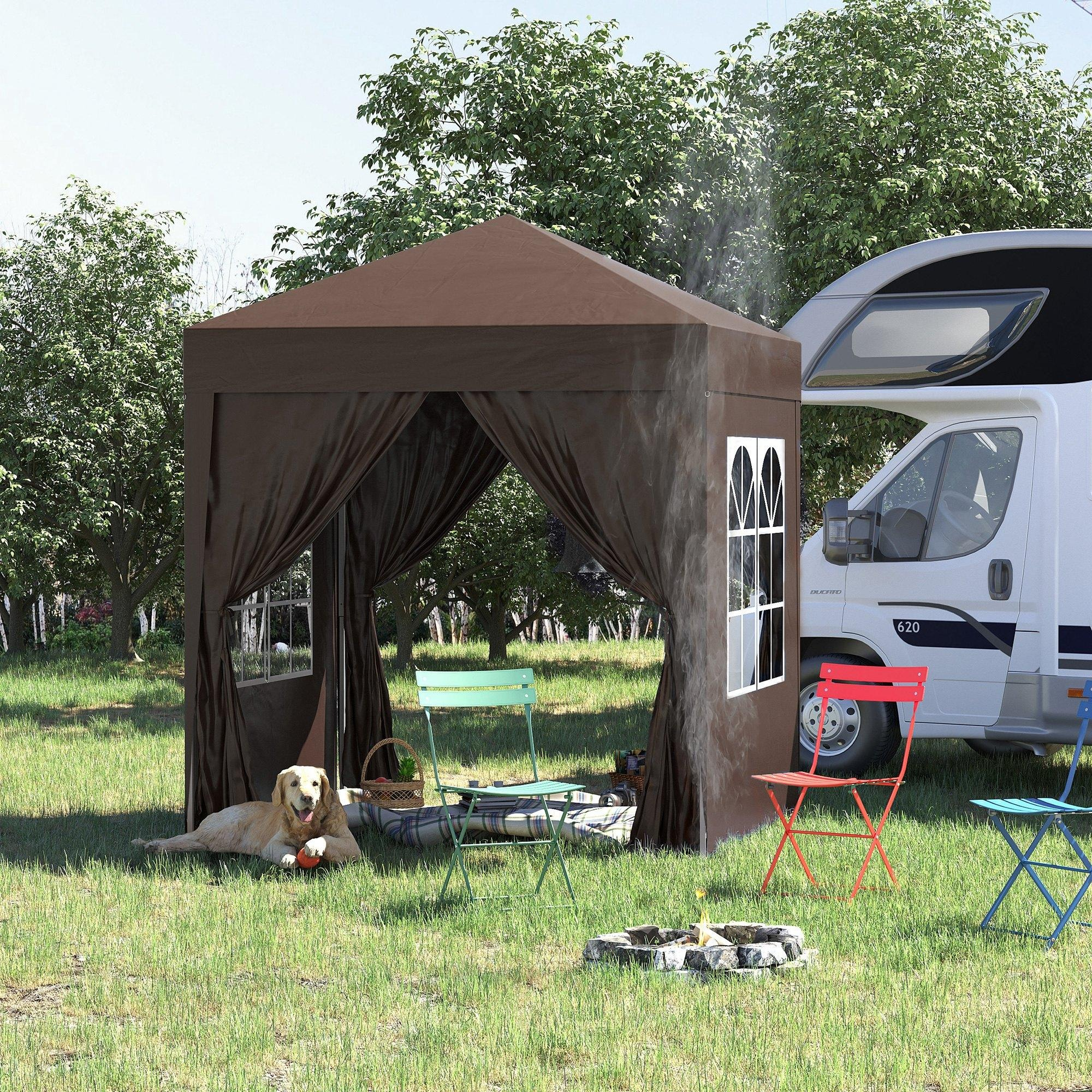 Ein Hund liegt vor einem braunen Pavillon neben einem Wohnmobil. Sitzgelegenheiten und Lagerfeuer sind im Gras.