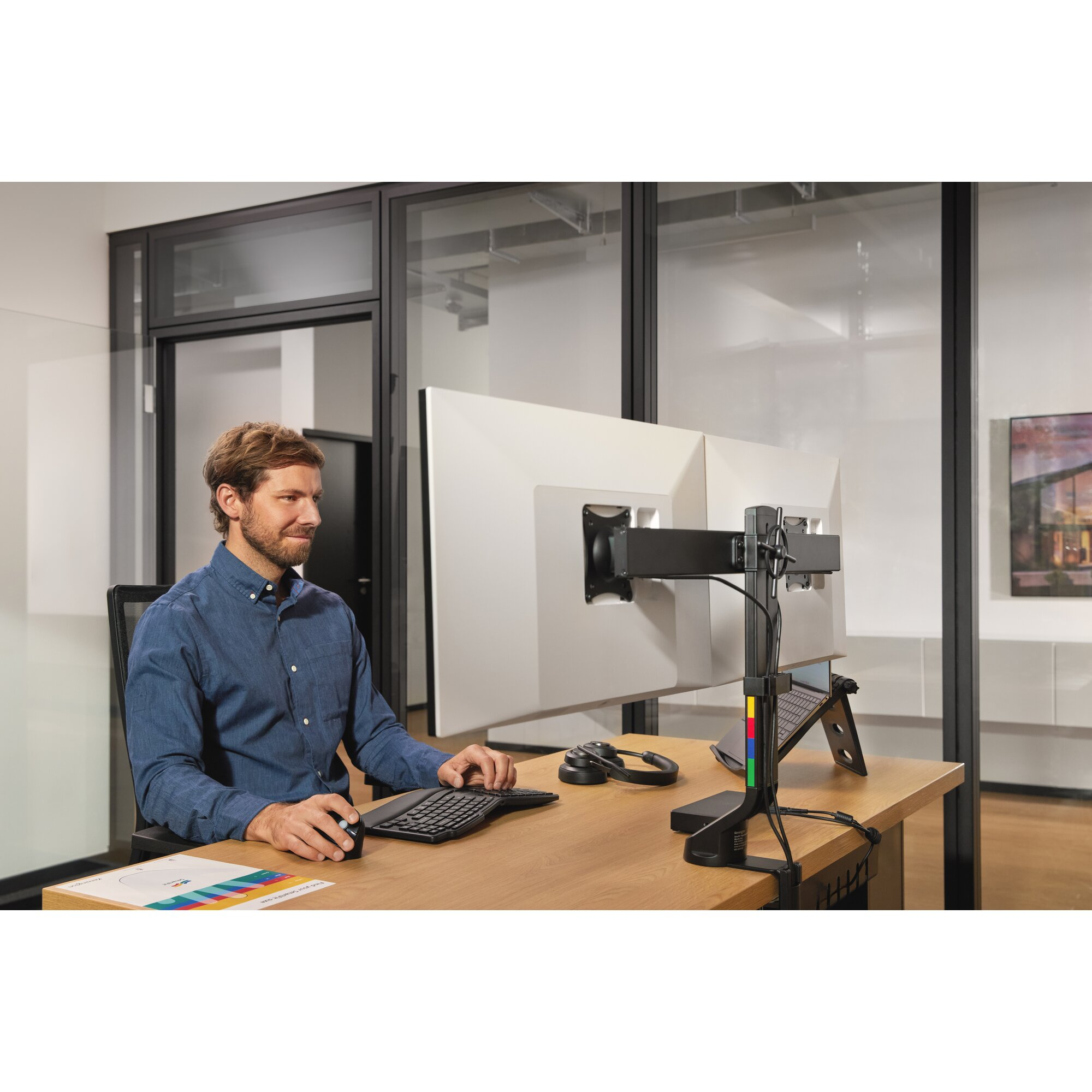 Ein Mann sitzt an einem Schreibtisch und tippt auf einer Tastatur. Ein Monitor ist montiert.