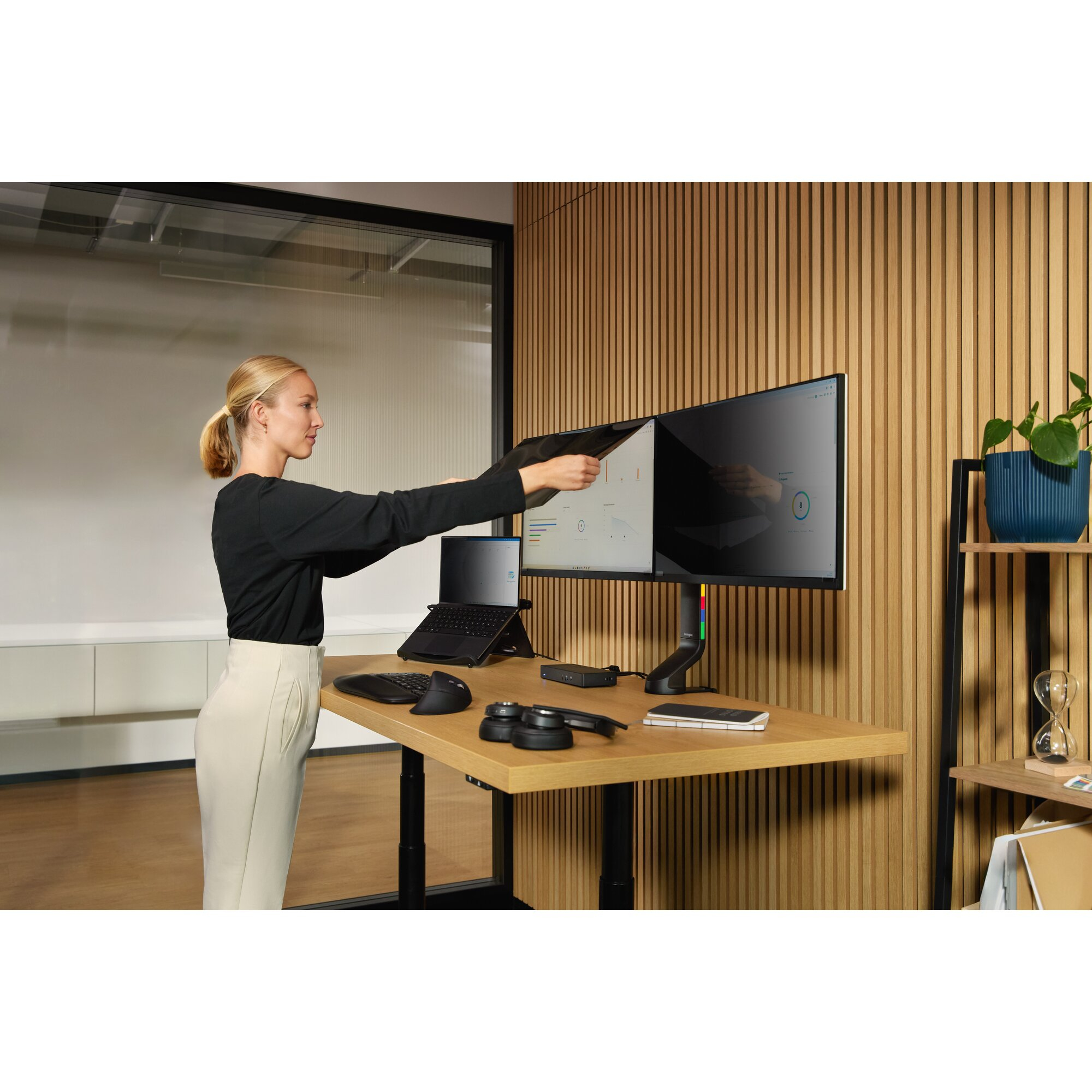 Frau in Schwarz klebt einen Sichtschutz auf einen Monitor über einem Schreibtisch.