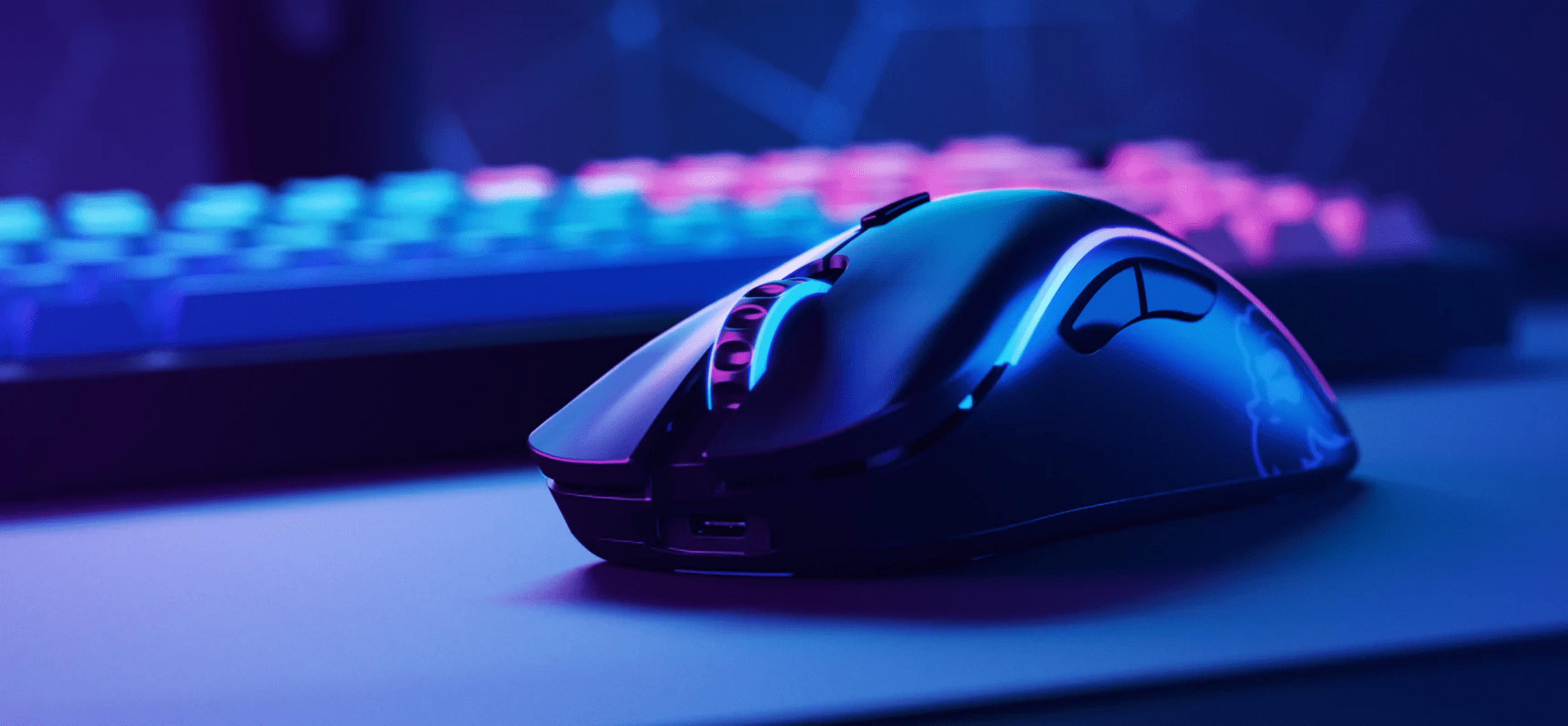 Czarna mysz gamingowa z niebieskim i fioletowym podświetleniem, obok klawiatury.