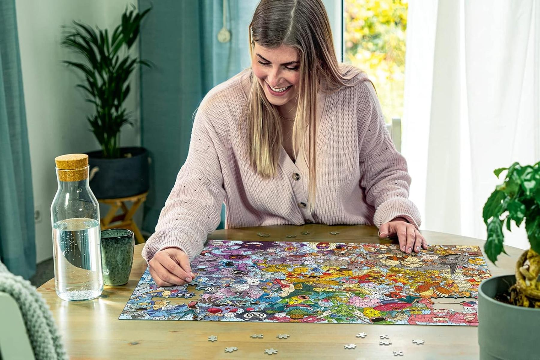 Kobieta siedzi przy stole i układa kolorowe puzzle. Obok butelka z wodą.
