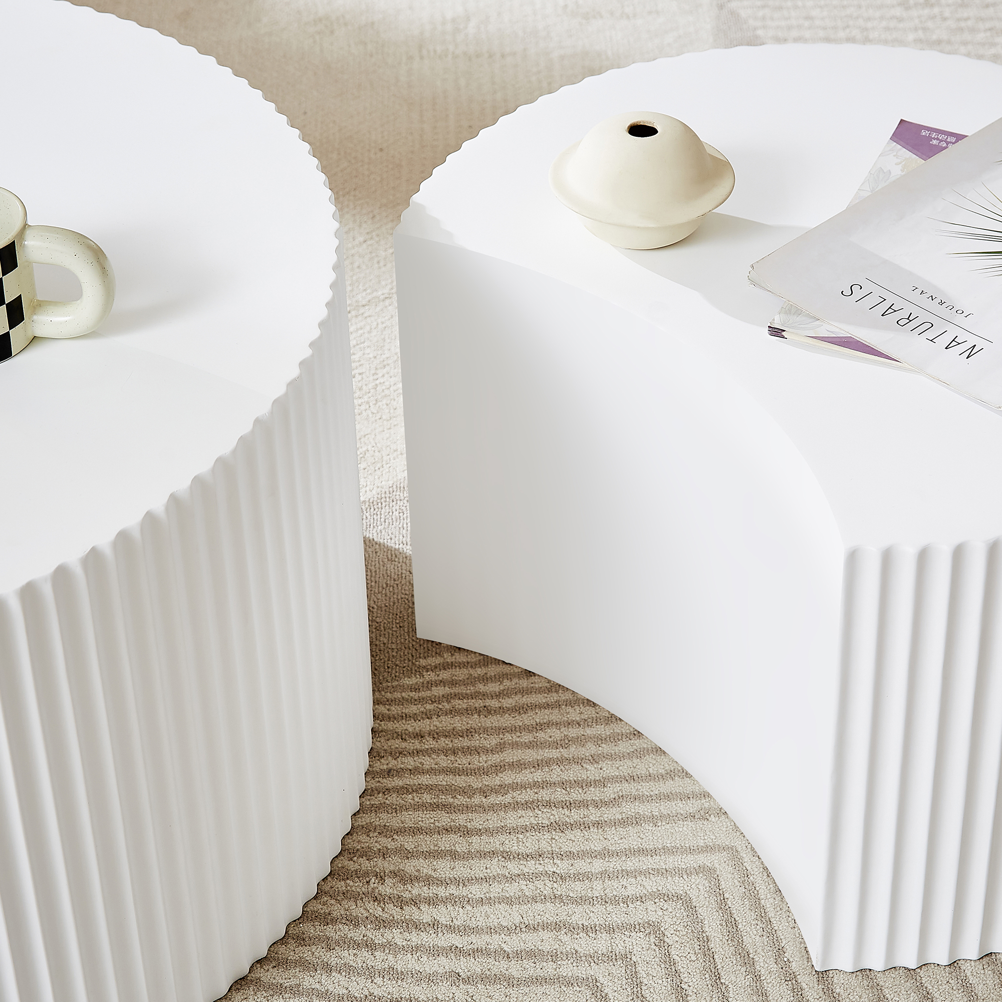 Zwei weiße Tische mit geriffelten Seiten. Einer hat eine Tasse, der andere eine Vase und Zeitschriften.