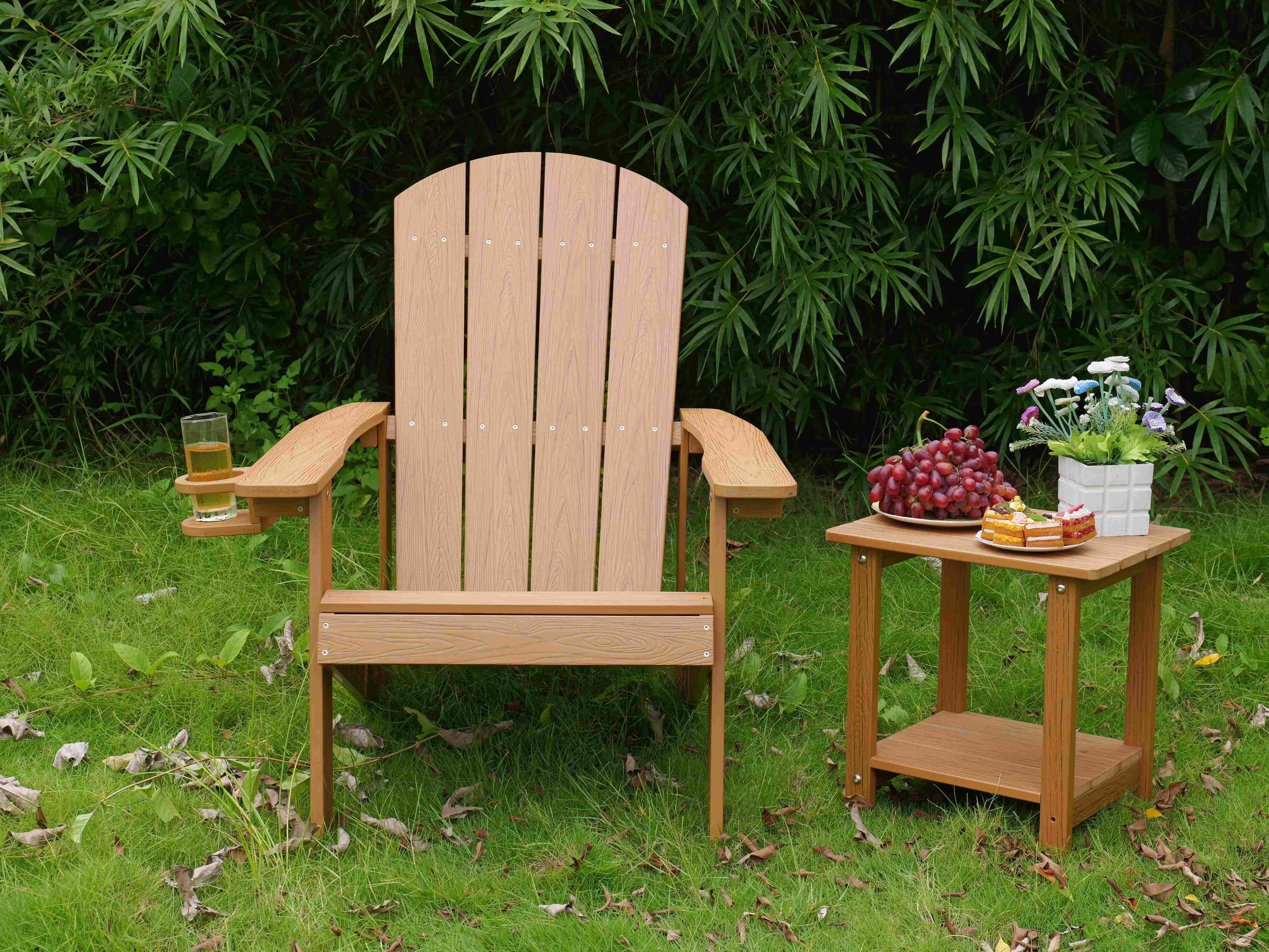 Ein Holzstuhl mit Getränkehalter steht im Gras neben einem Tisch mit Trauben und Kuchen.