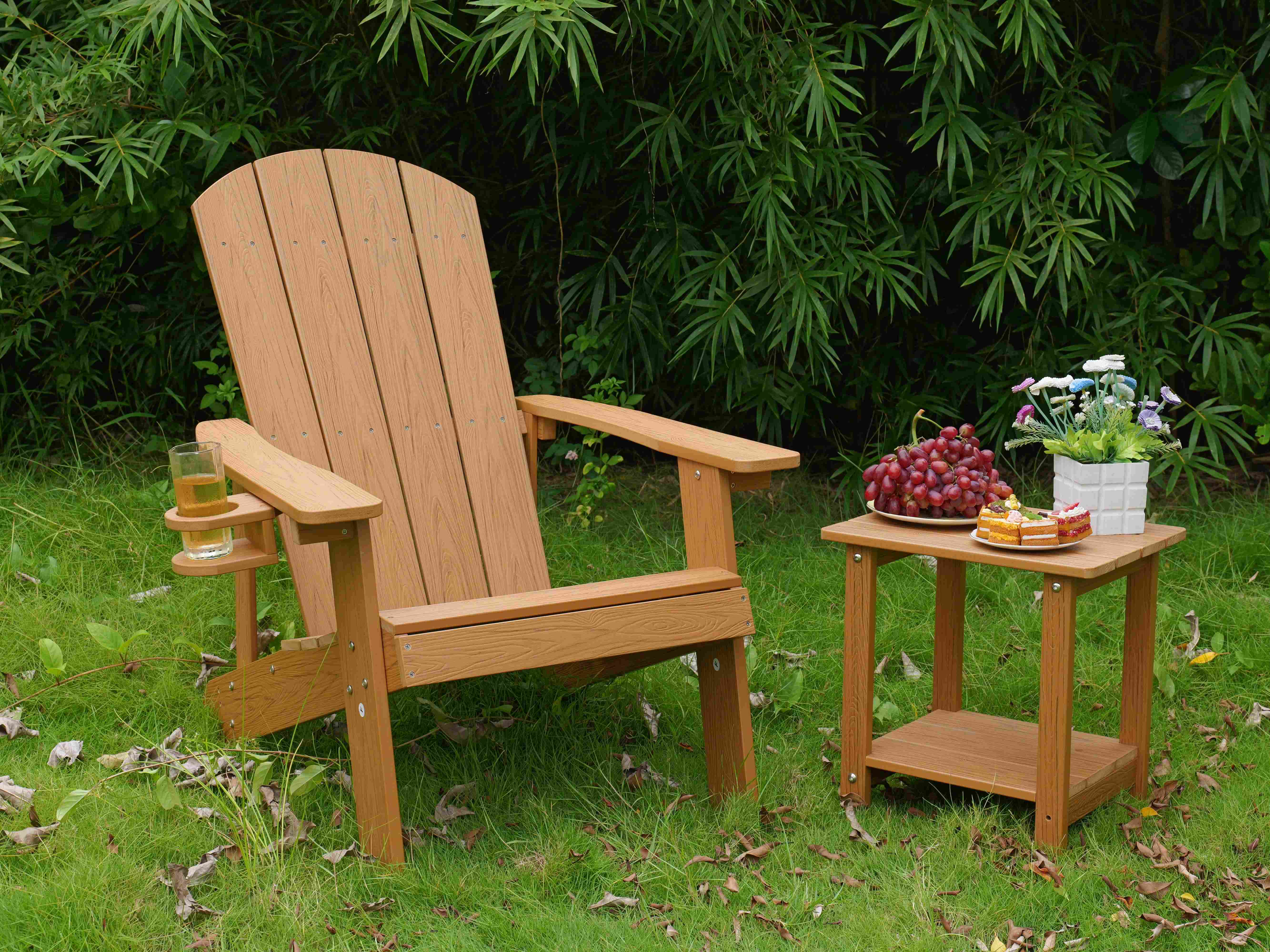 Ein Holzstuhl und ein Beistelltisch mit Snacks und Blumen auf Gras vor Bambushintergrund.