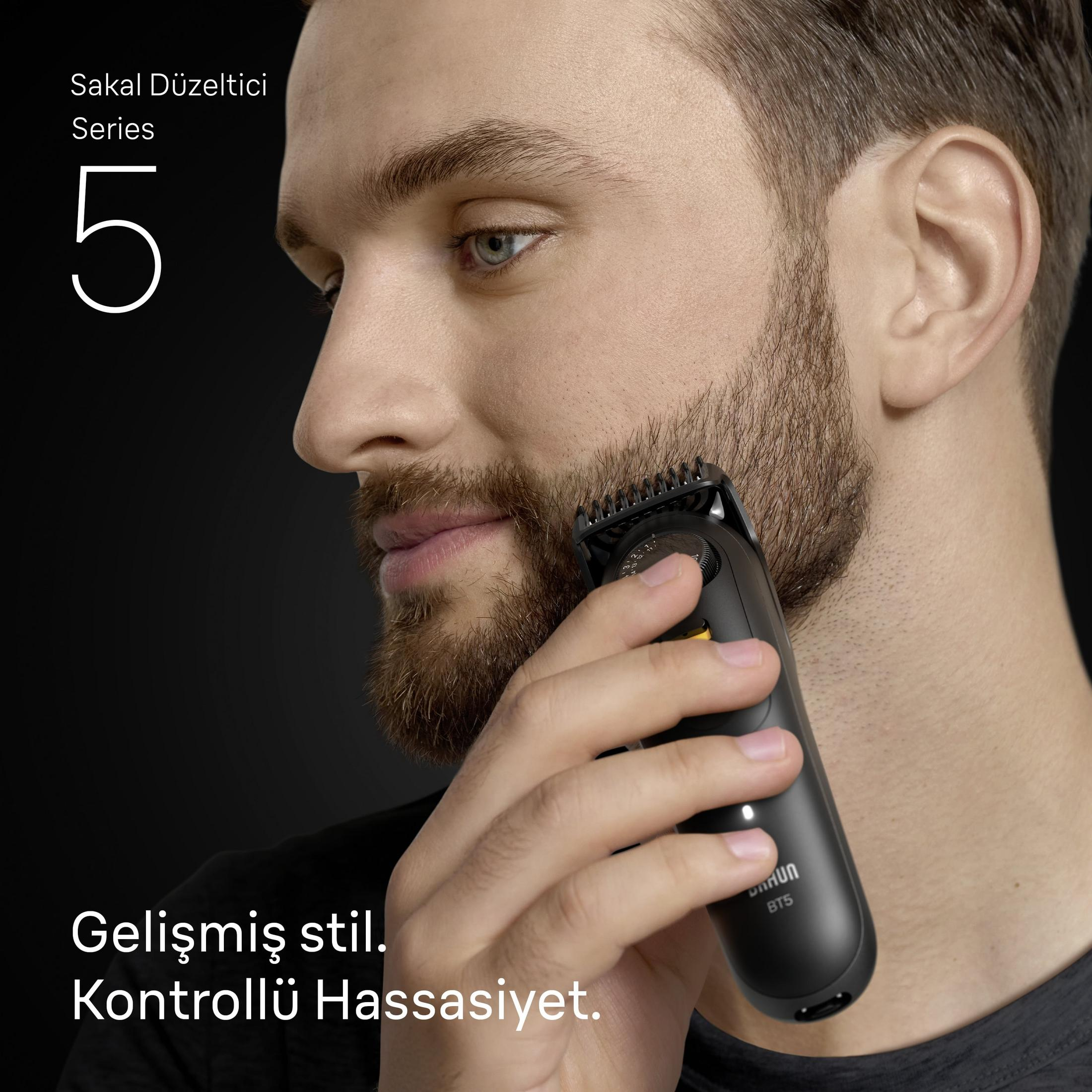 Ein Mann trimmt seinen Bart mit einem schwarzen Trimmer auf dunklem Hintergrund.