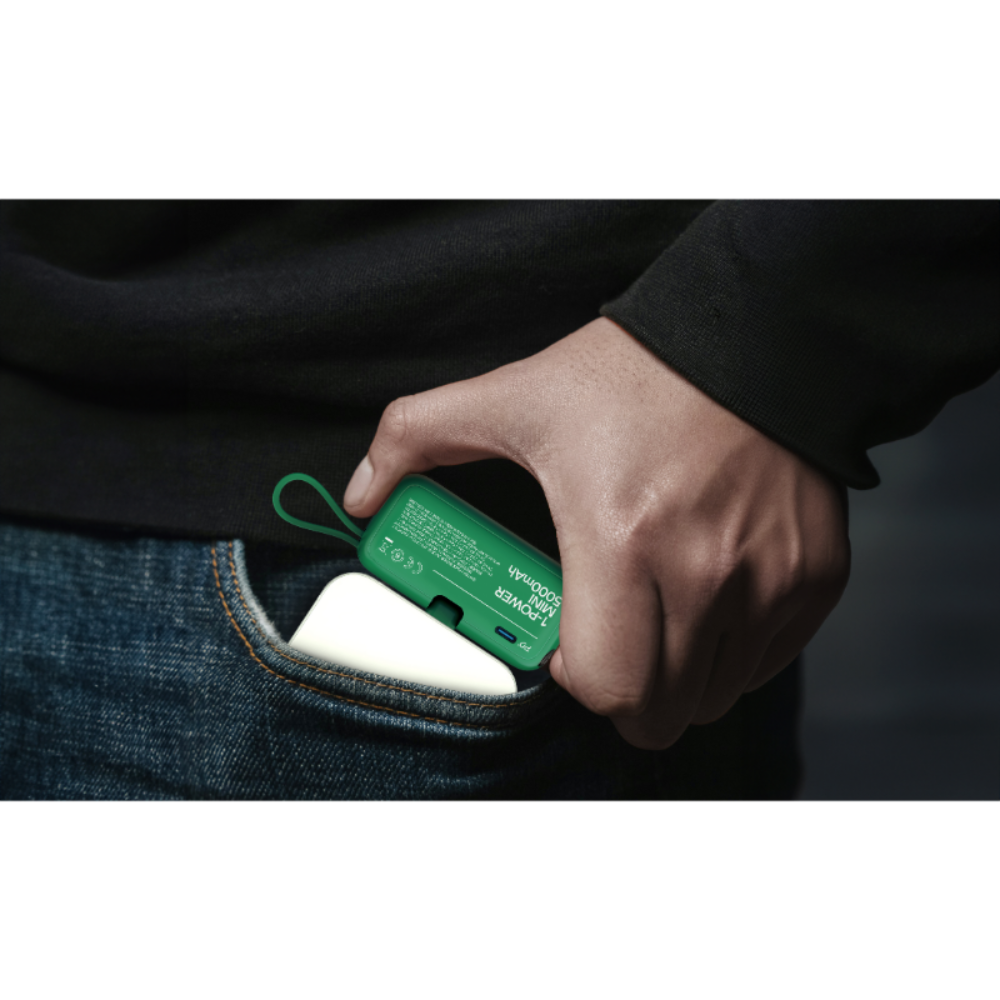Bir el, yeşil 5000 mAh'lik şarj cihazını kot cebine yerleştiriyor.