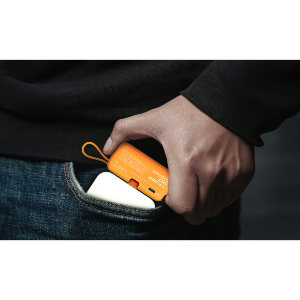 Bir el, kot cepine yerleştirilen turuncu bir powerbank tutuyor.