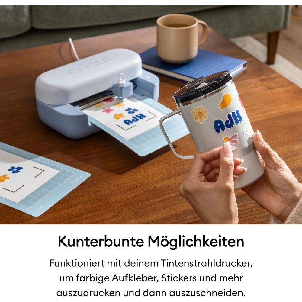 Una máquina Cricut corta pegatinas coloridas mientras una persona pone pegatinas en una taza.