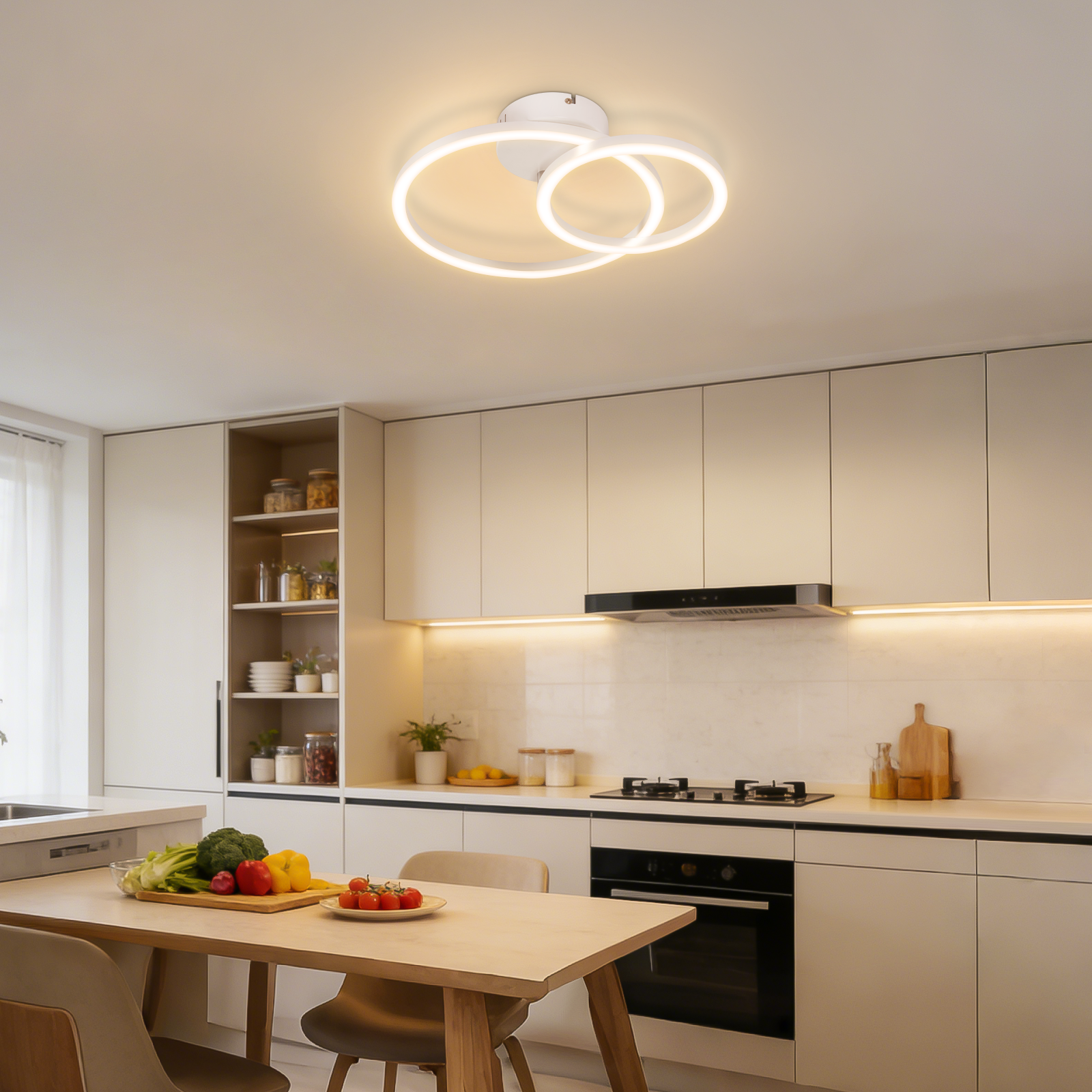 Cucina moderna con mobili bianchi, piano cottura e tavolo da pranzo con verdure.